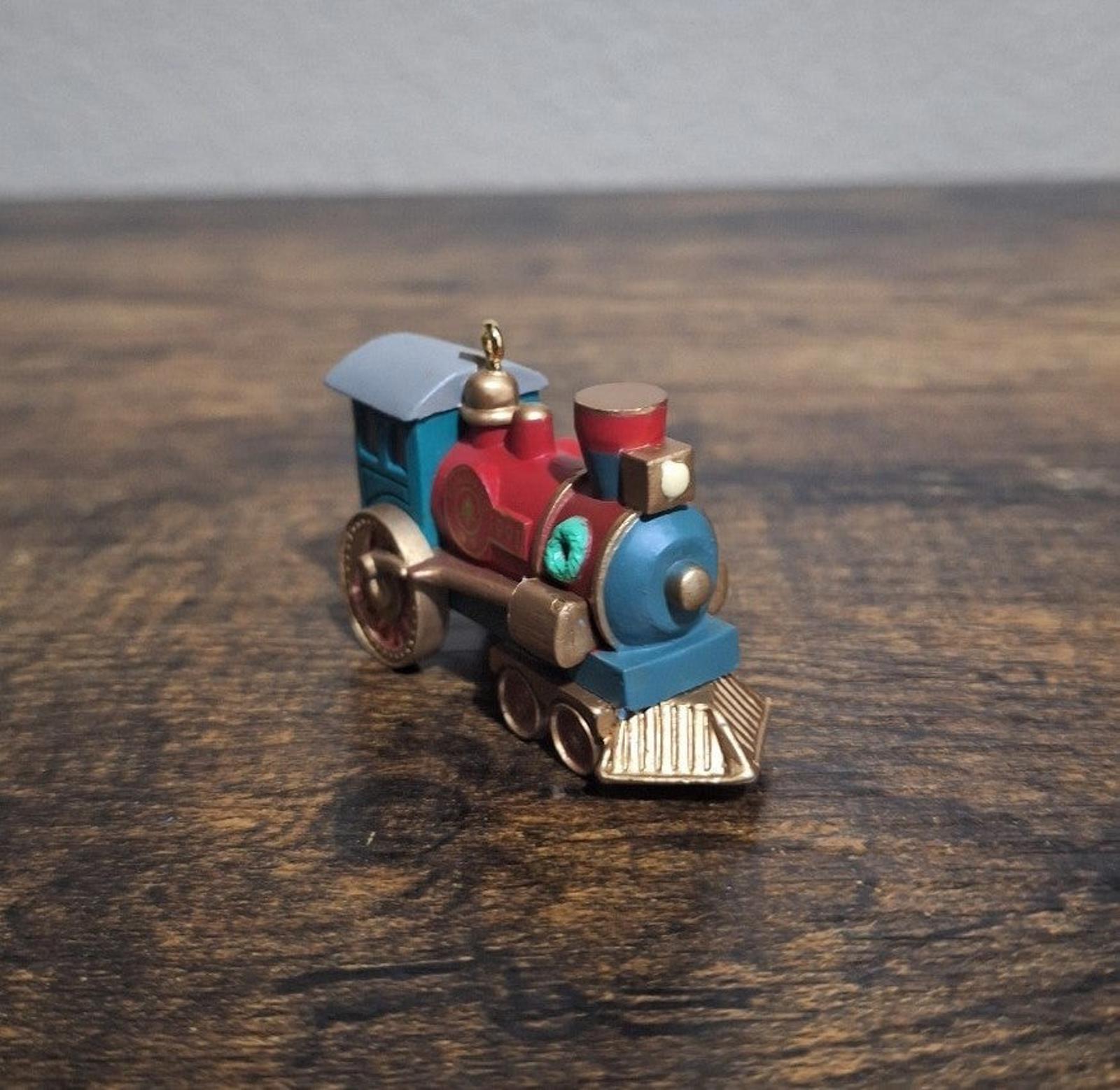 Blue and red train locomotive ornament, three-quarter view with gold bell and front wheels