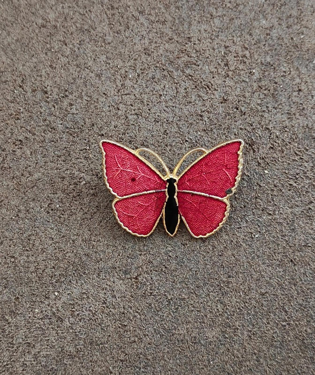 Red butterfly enamel brooch with gold-tone wing edges and black body, on fabric.