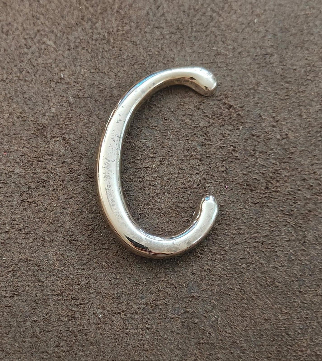 Silver tone letter C monogram pin/brooch lying flat, curved open C form with shine.