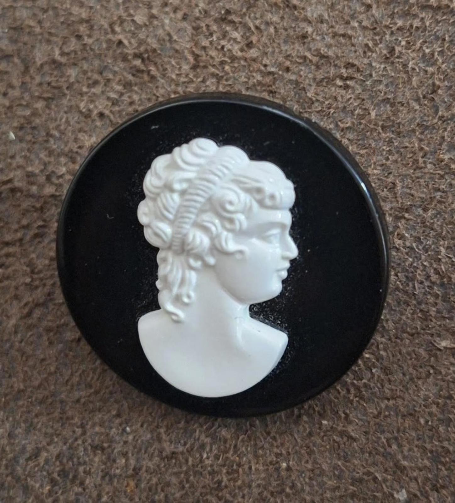 Black round cameo brooch featuring raised white woman's profile in side view