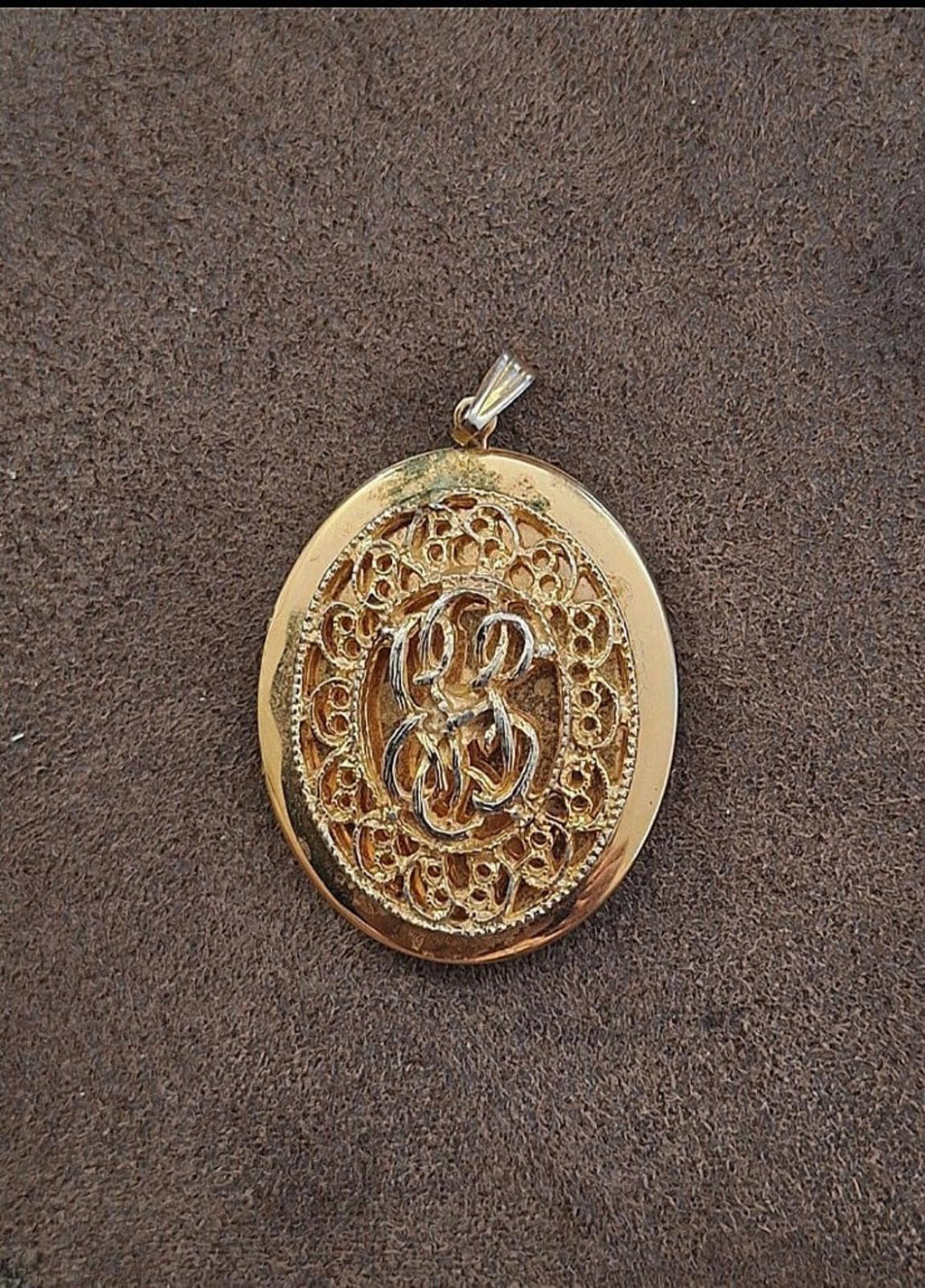Gold tone oval filigree locket pendant front with ornate inner design and bail.