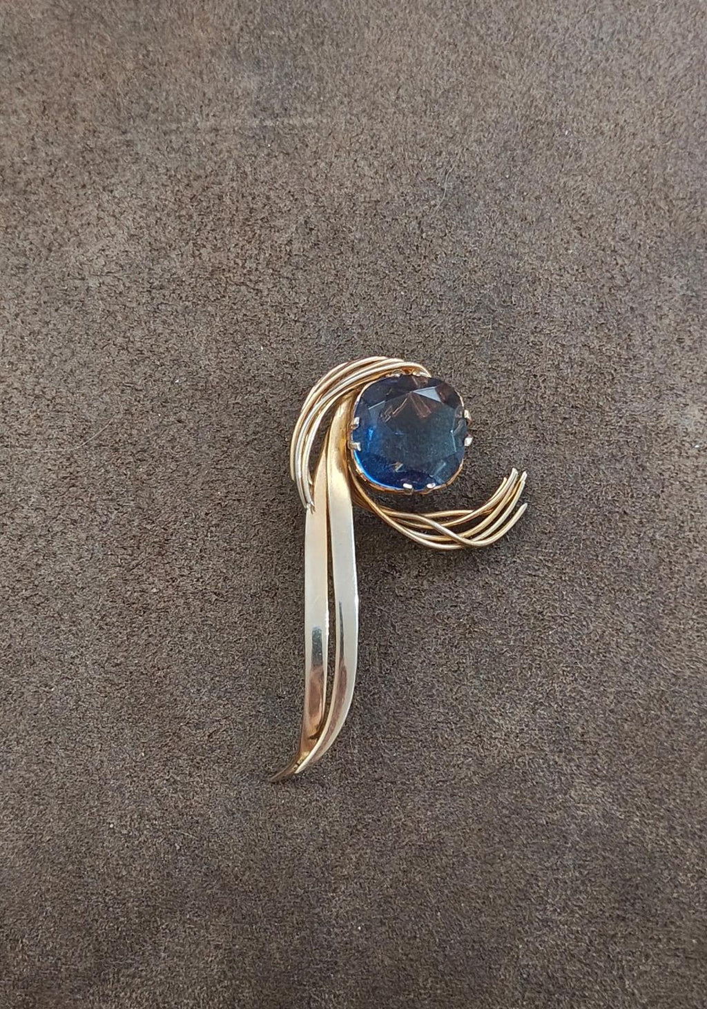 Gold-tone abstract brooch pin with large blue gemstone and sculpted swirl setting
