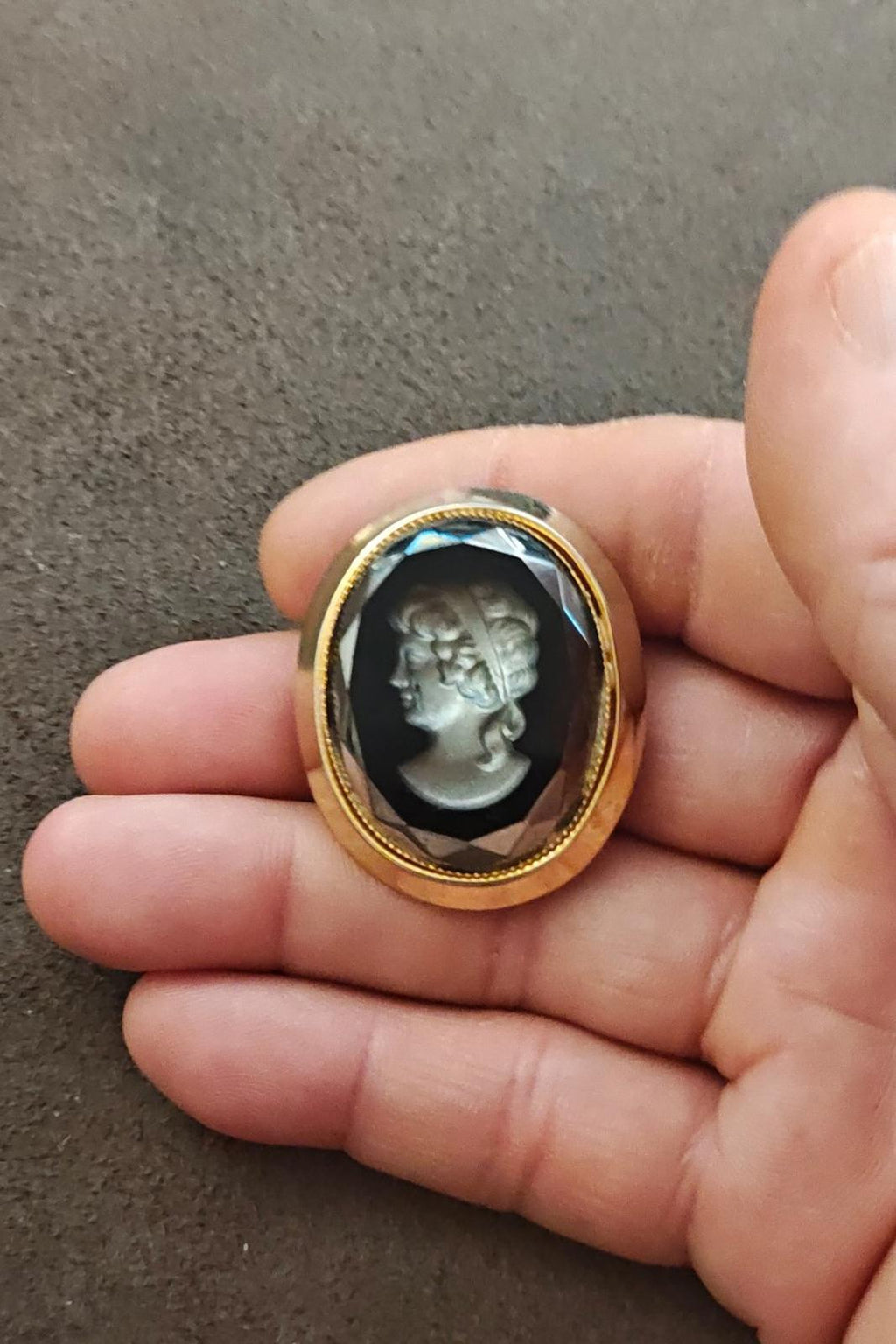 Handheld oval cameo brooch with gold bezel and black setting, silver relief profile woman