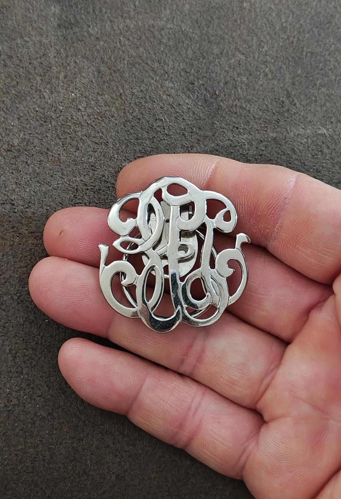 Silver-tone monogram scarf clip held in hand, ornate cutout letters