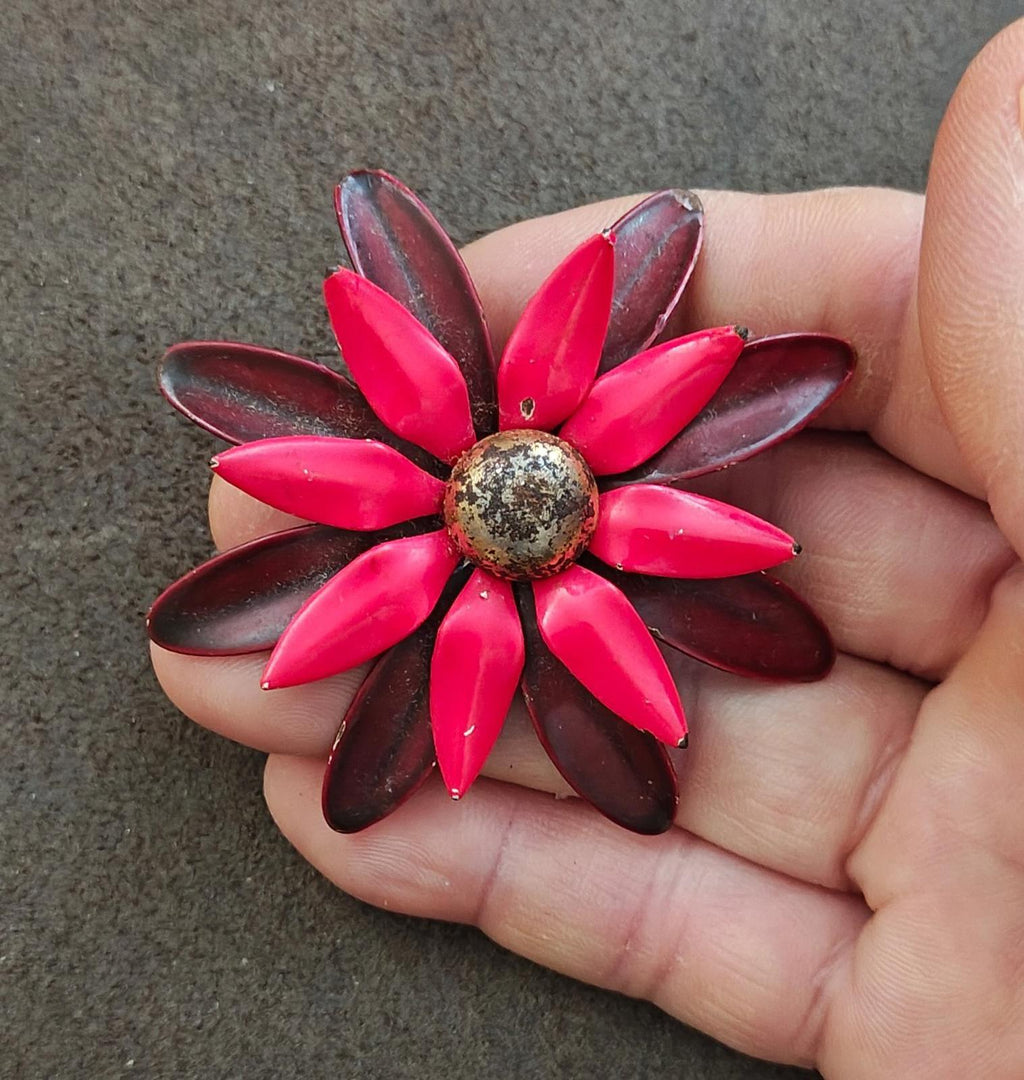 Red and burgundy daisy enamel pin brooch on open palm, front details visible