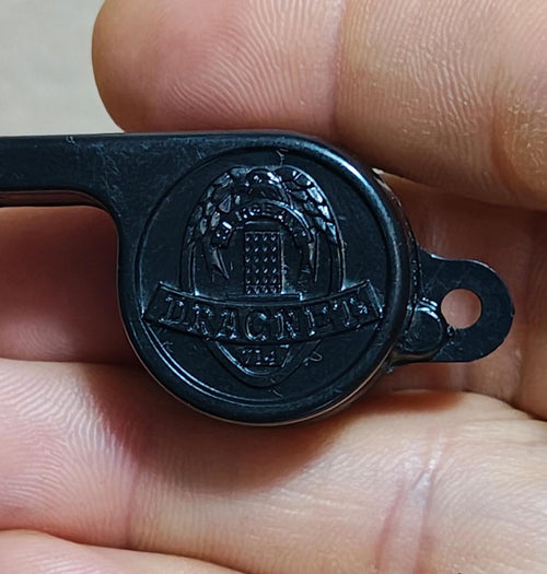 Black whistle head with engraved emblem and side tube, close-up in hand.