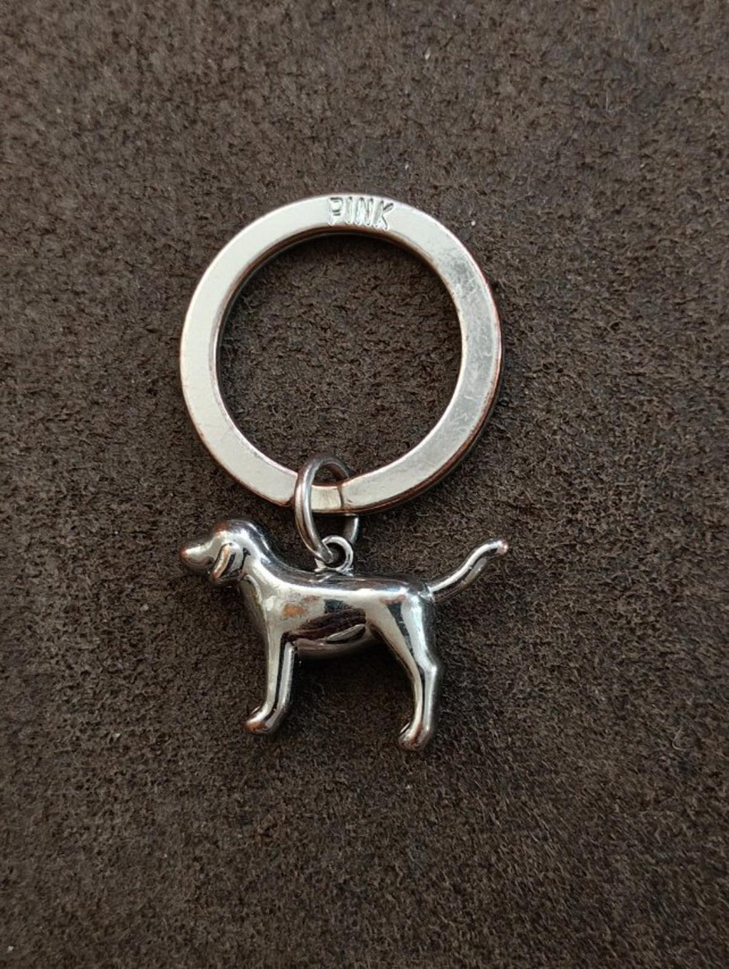 Silver tone dog charm keychain on surface, Pink logo ring with dog pendant
