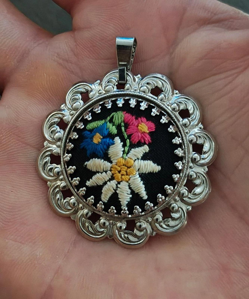 Silver filigree round pendant on a bail, black embroidered flower with bright accents.