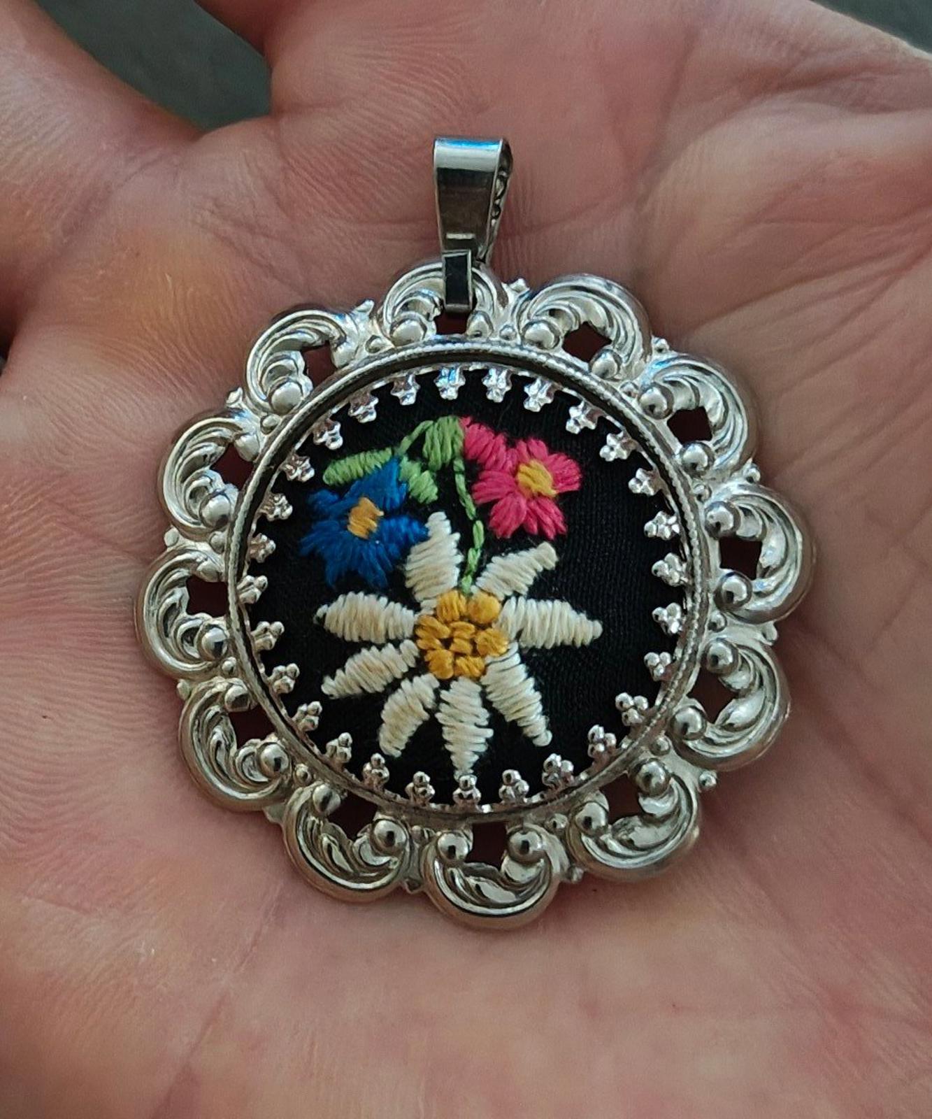 Silver filigree round pendant on a bail, black embroidered flower with bright accents.