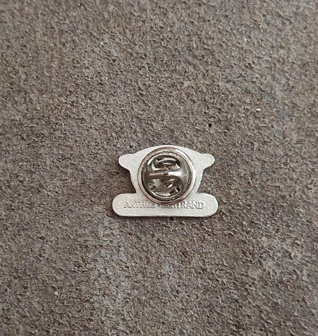 Silver-tone pin back with clasp and maker text on gray fabric