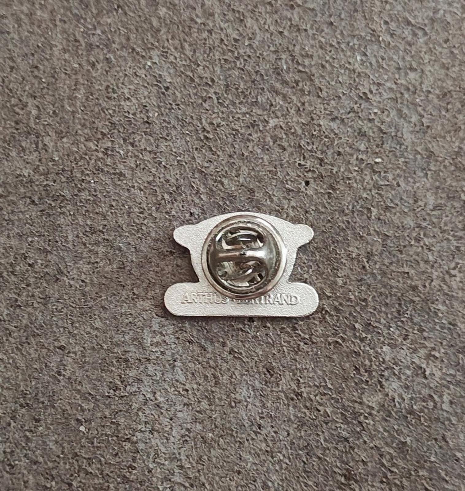 Silver-tone pin back with clasp and maker text on gray fabric