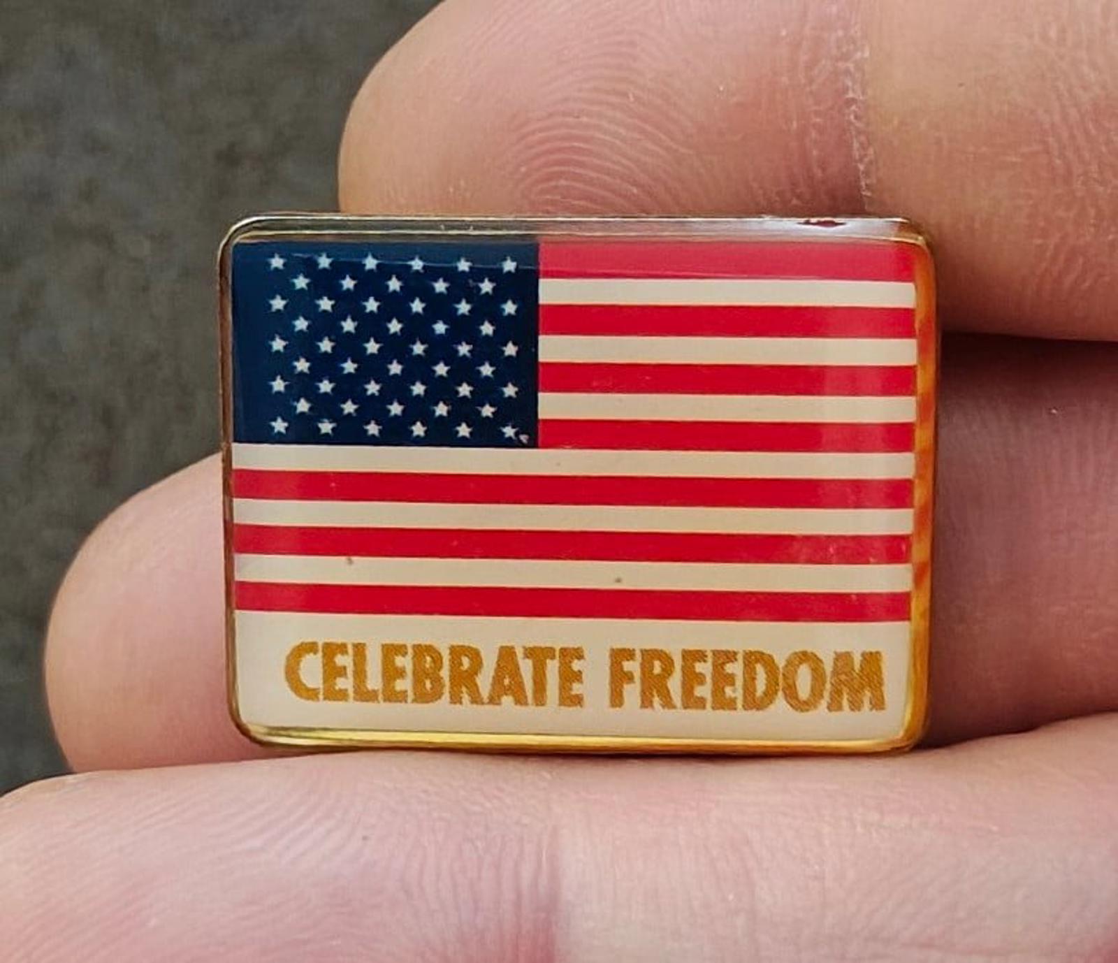 Gold-tone rectangular patriotic flag pin with “CELEBRATE FREEDOM” text