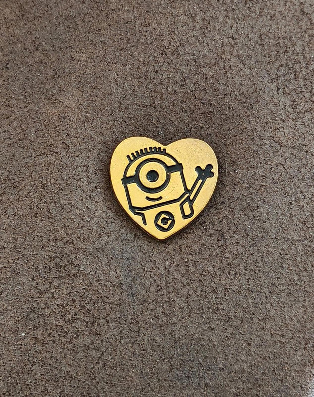 Gold heart-shaped Minion pin on gray surface, front artwork visible