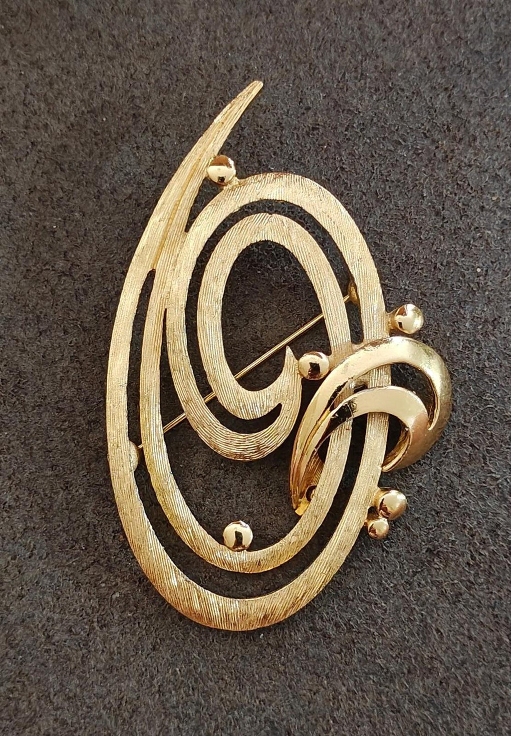 Gold tone oval brooch pin with double swirl motif and hinged pin mechanism