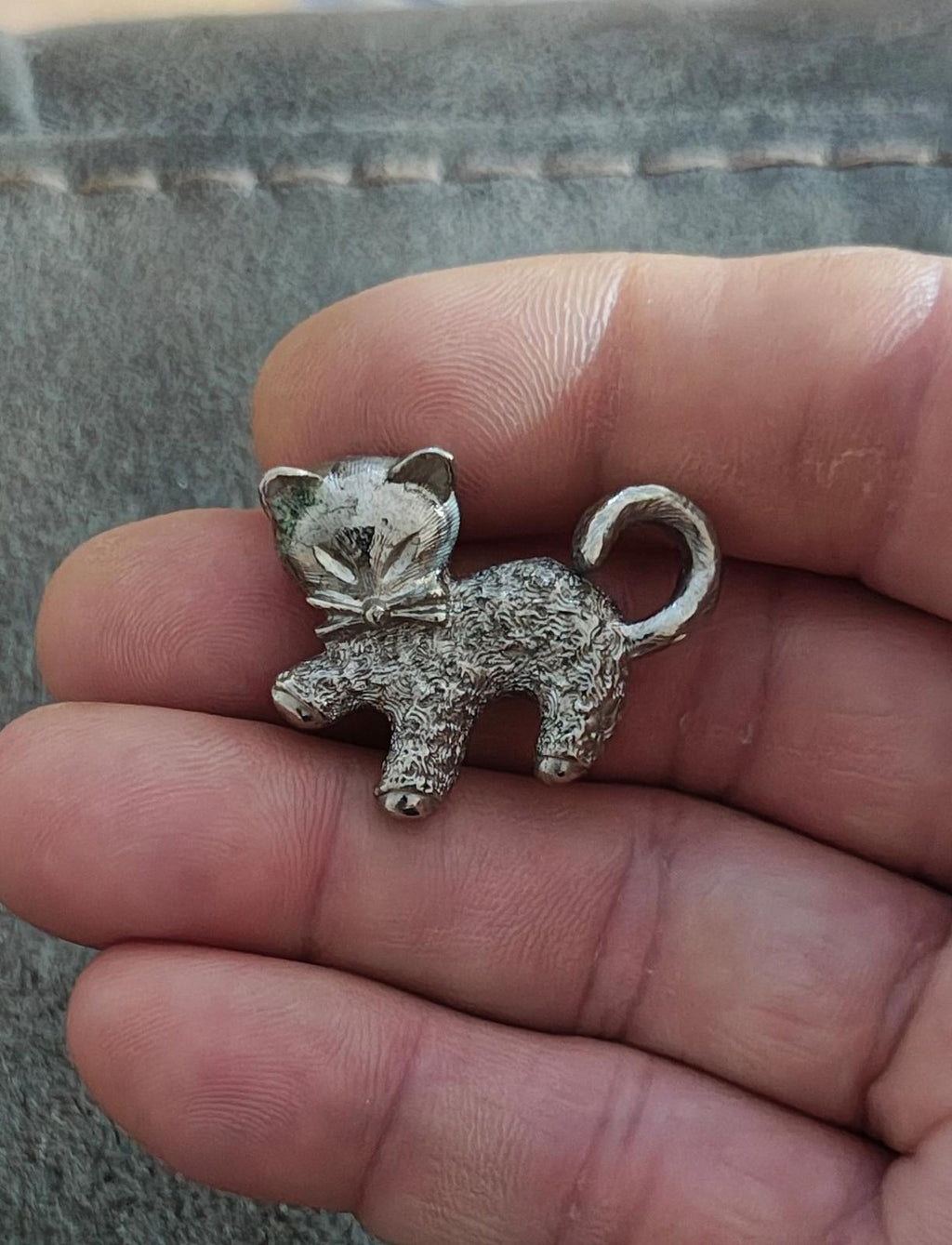 Silver-tone cat brooch pin with textured body, bow at neck, curled tail.