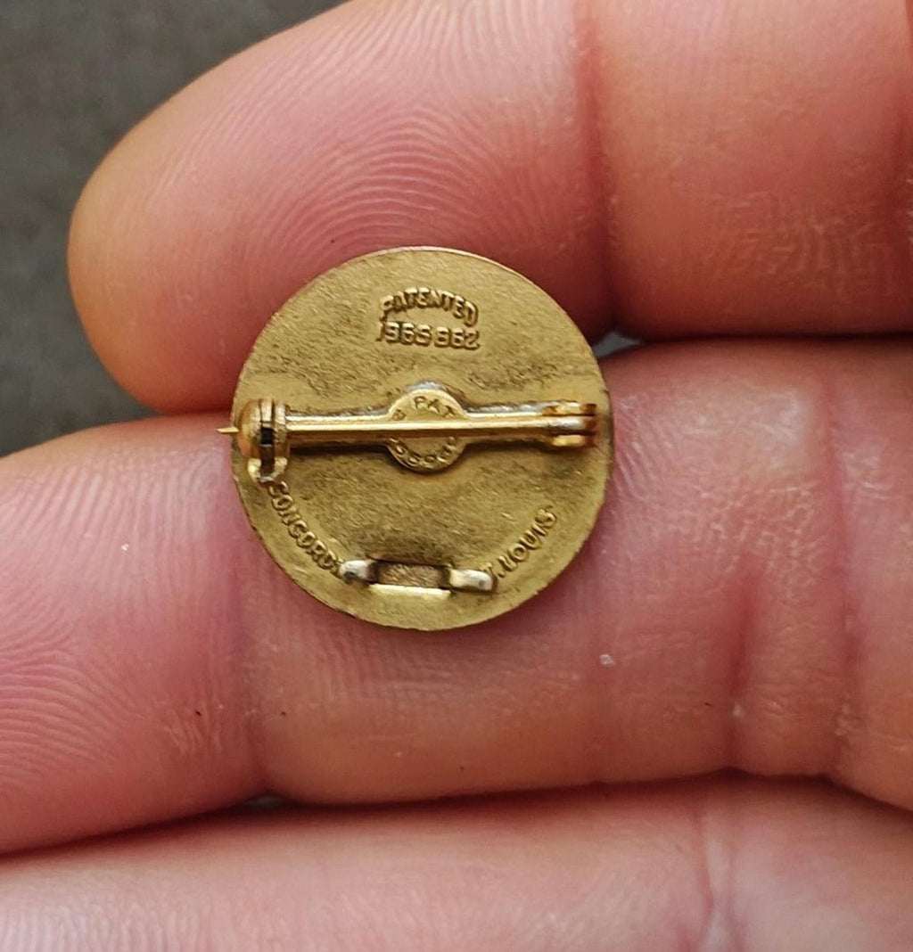 Back of vintage gold-tone award pin with metal pin clasp on round medallion
