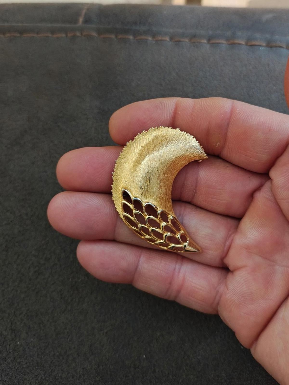 Gold tone feather plume brooch in hand, curved plume with openwork mesh edge