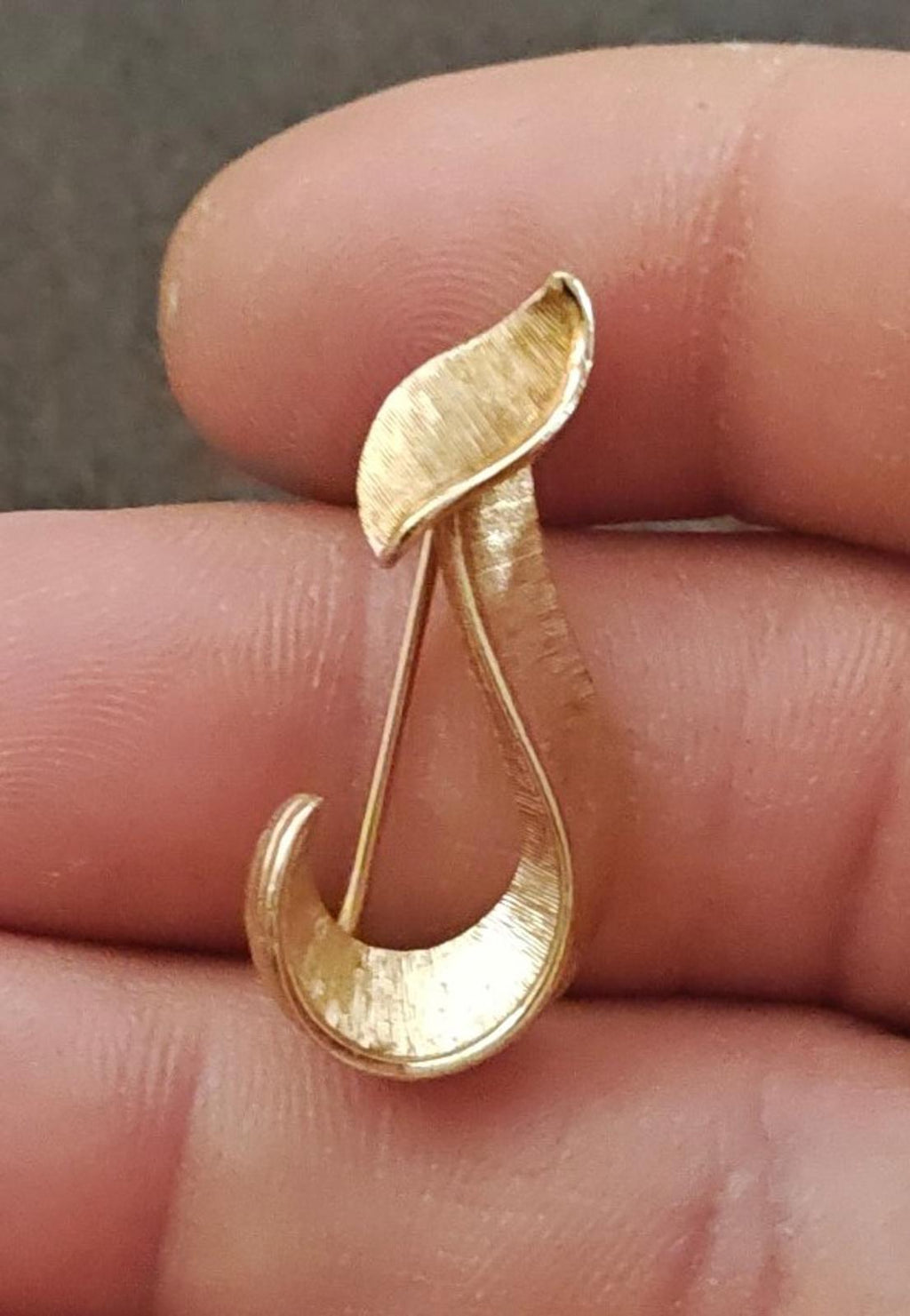 Gold-tone monogram J brooch close-up on fingertips, textured finish