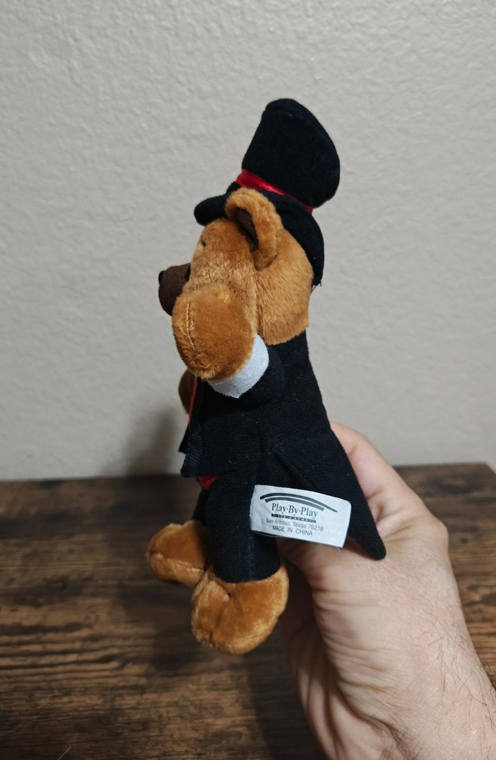 Plush bear back with black top hat, red band, and white label on tuxedo.