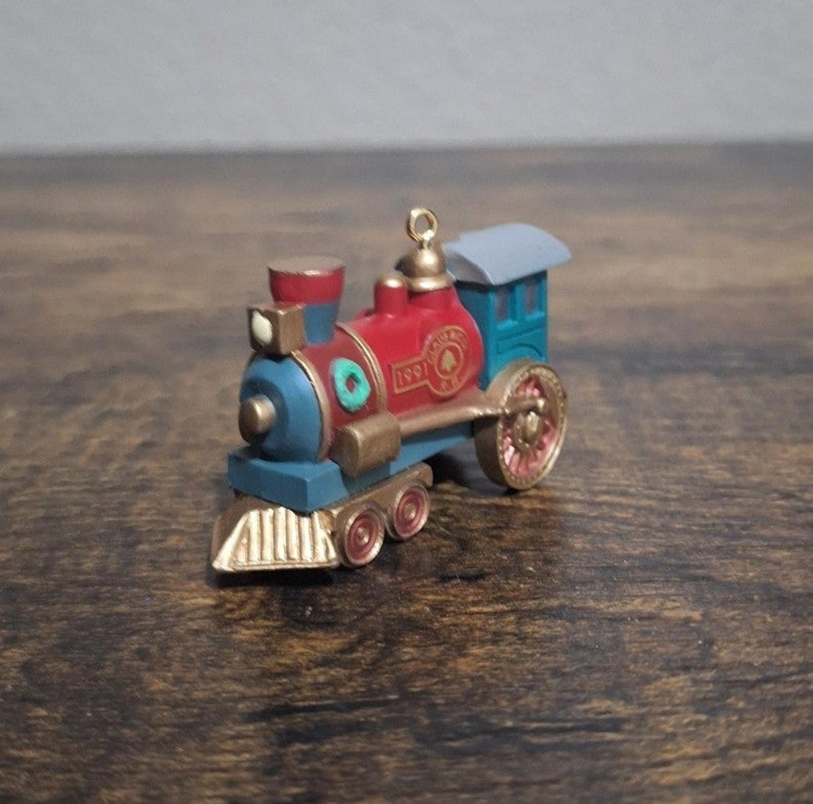 Blue and red train locomotive ornament, angled side view with gold bell and red badge