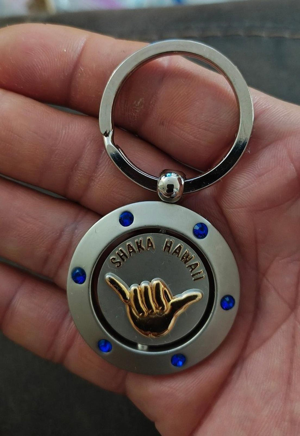 Round Shaka Hawaii keychain with blue jewel dots, gold hand emblem, and silver ring.