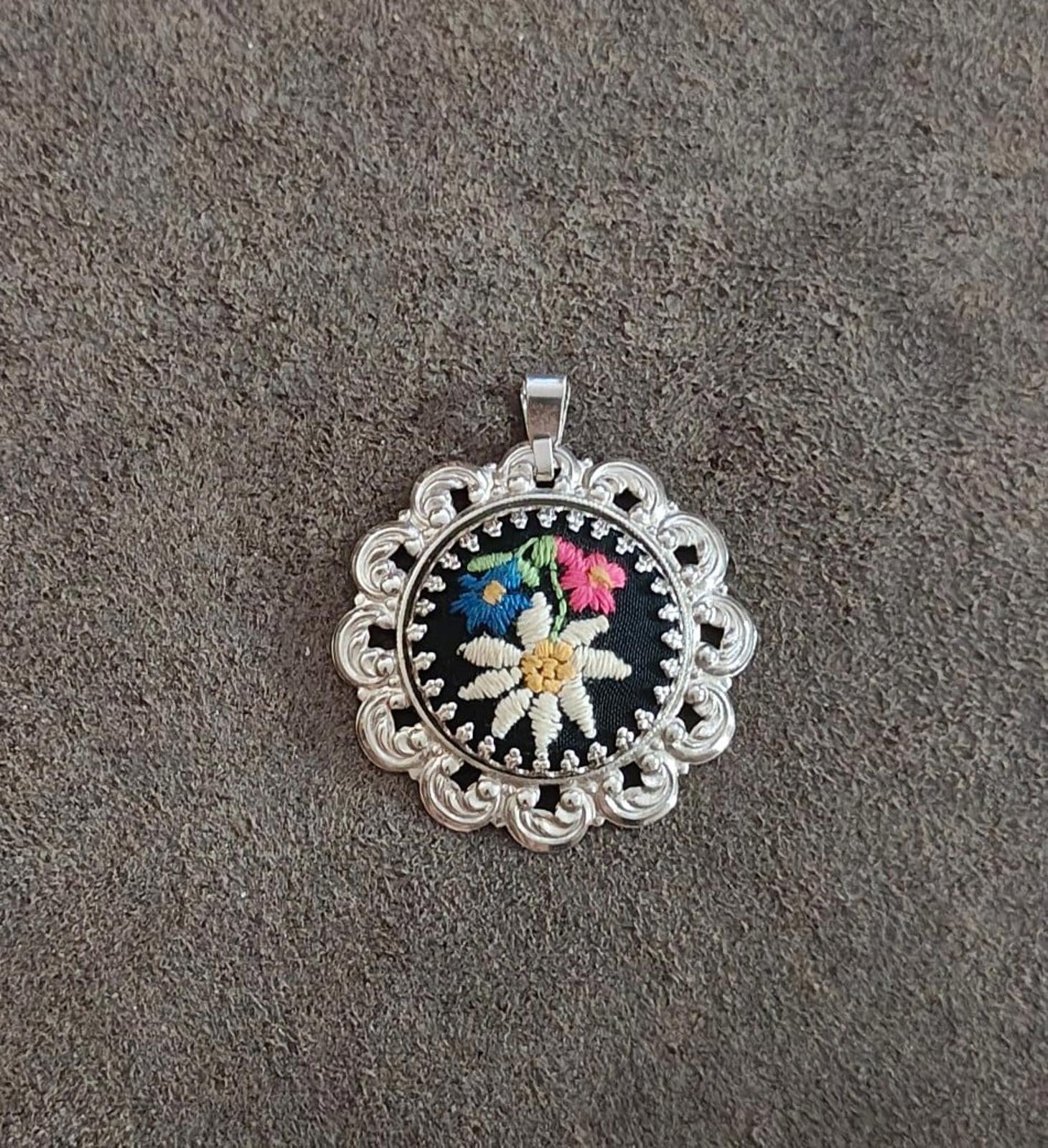 Silver filigree round pendant with black embroidered daisy-style flower and bail.