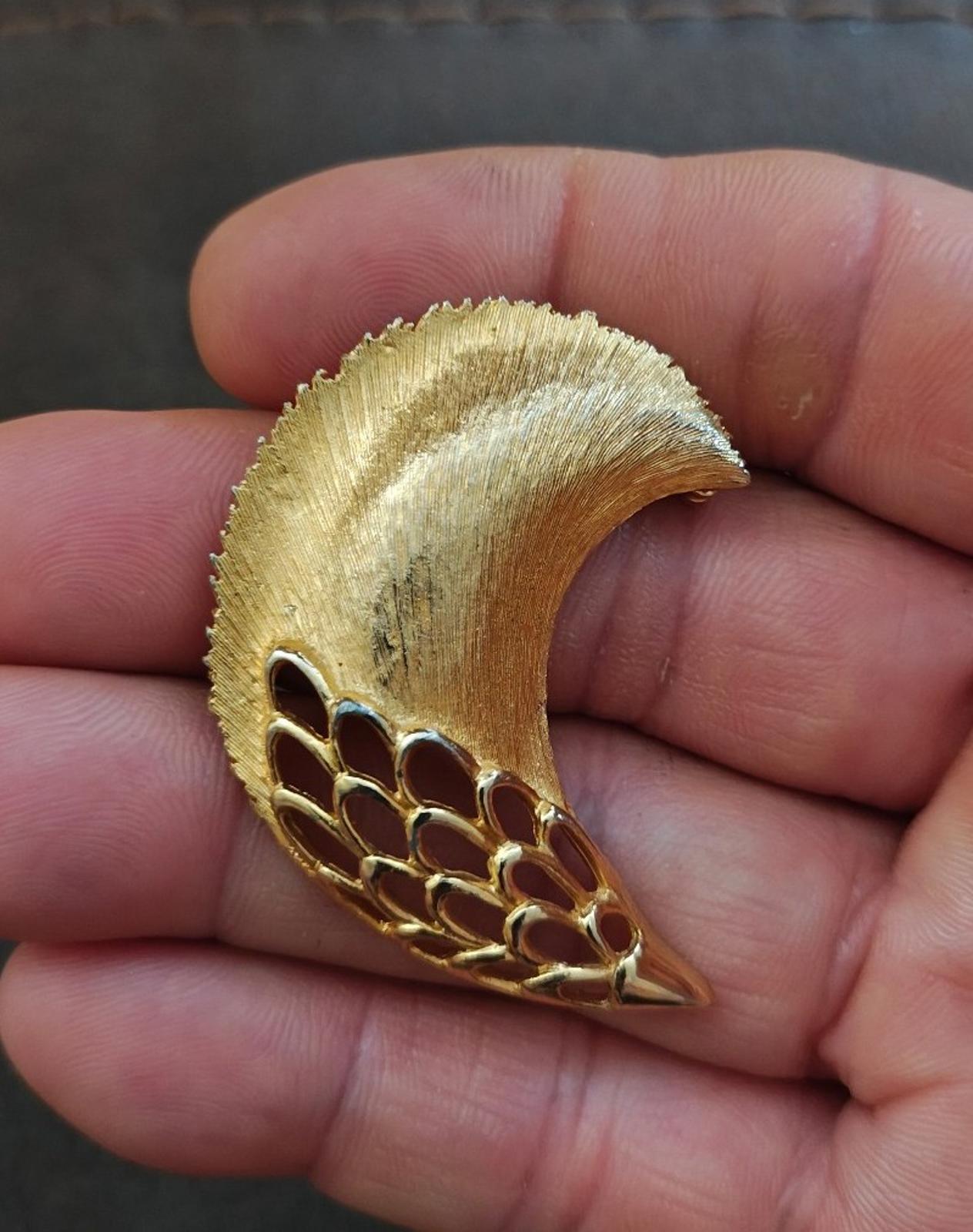 Gold tone textured feather plume brooch with cutout mesh tail, held in hand