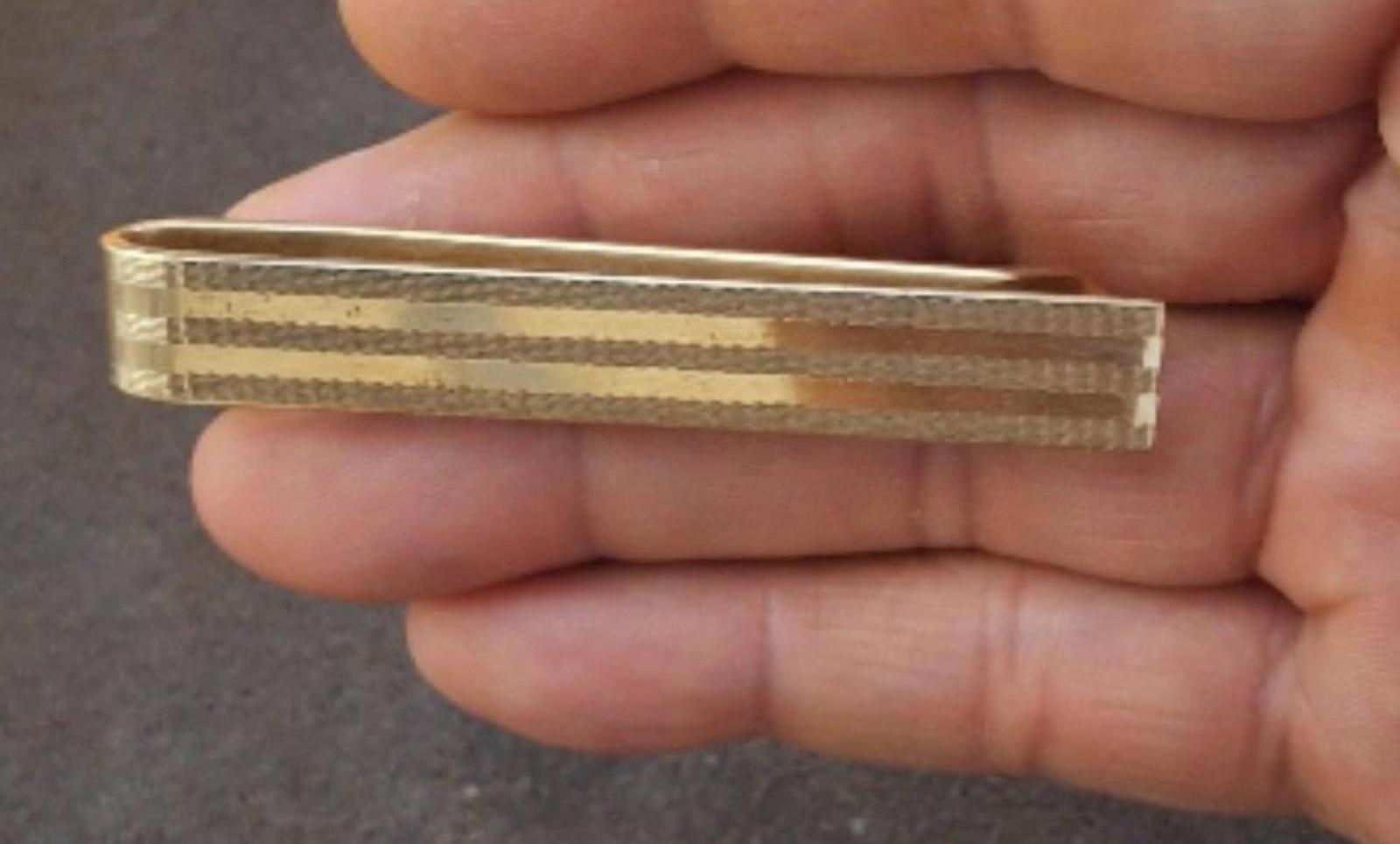 Gold tone tie bar clip with micro-patterned stripe texture along the face