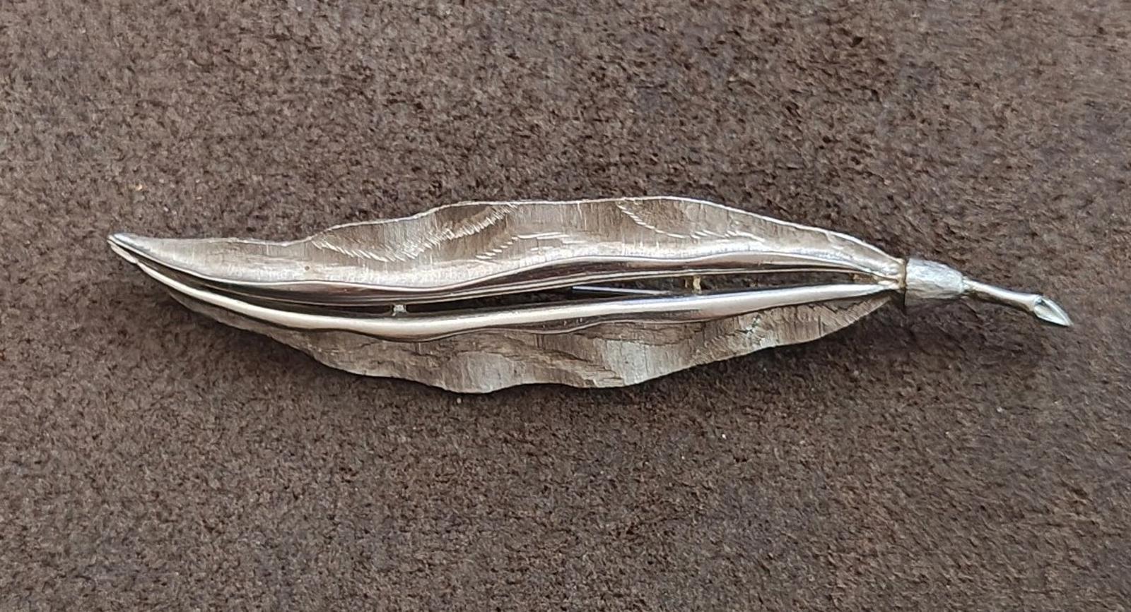 Silver tone hammered leaf brooch in side view with winglike ridges and pin