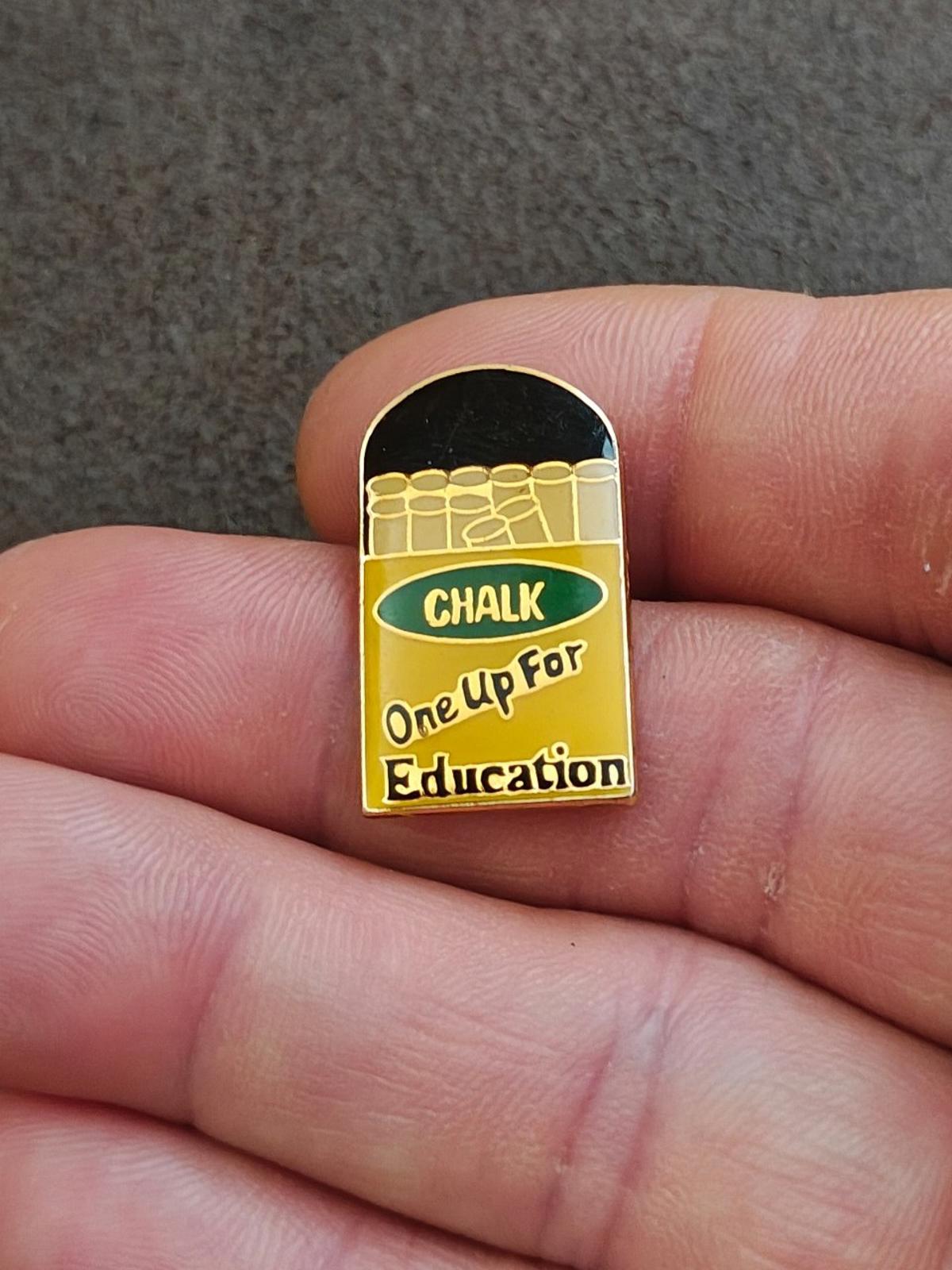 Close-up gold-tone enamel teacher pin with chalkboard text “CHALK / One Up For Education”