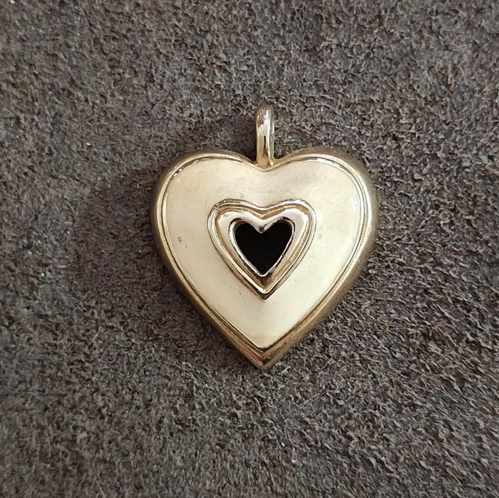 Gold tone heart pendant with white enamel and black heart inset, flat against dark fabric