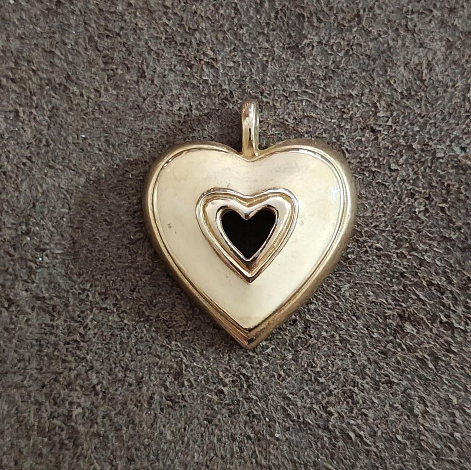 Gold tone heart pendant with white enamel and black heart inset, flat against dark fabric