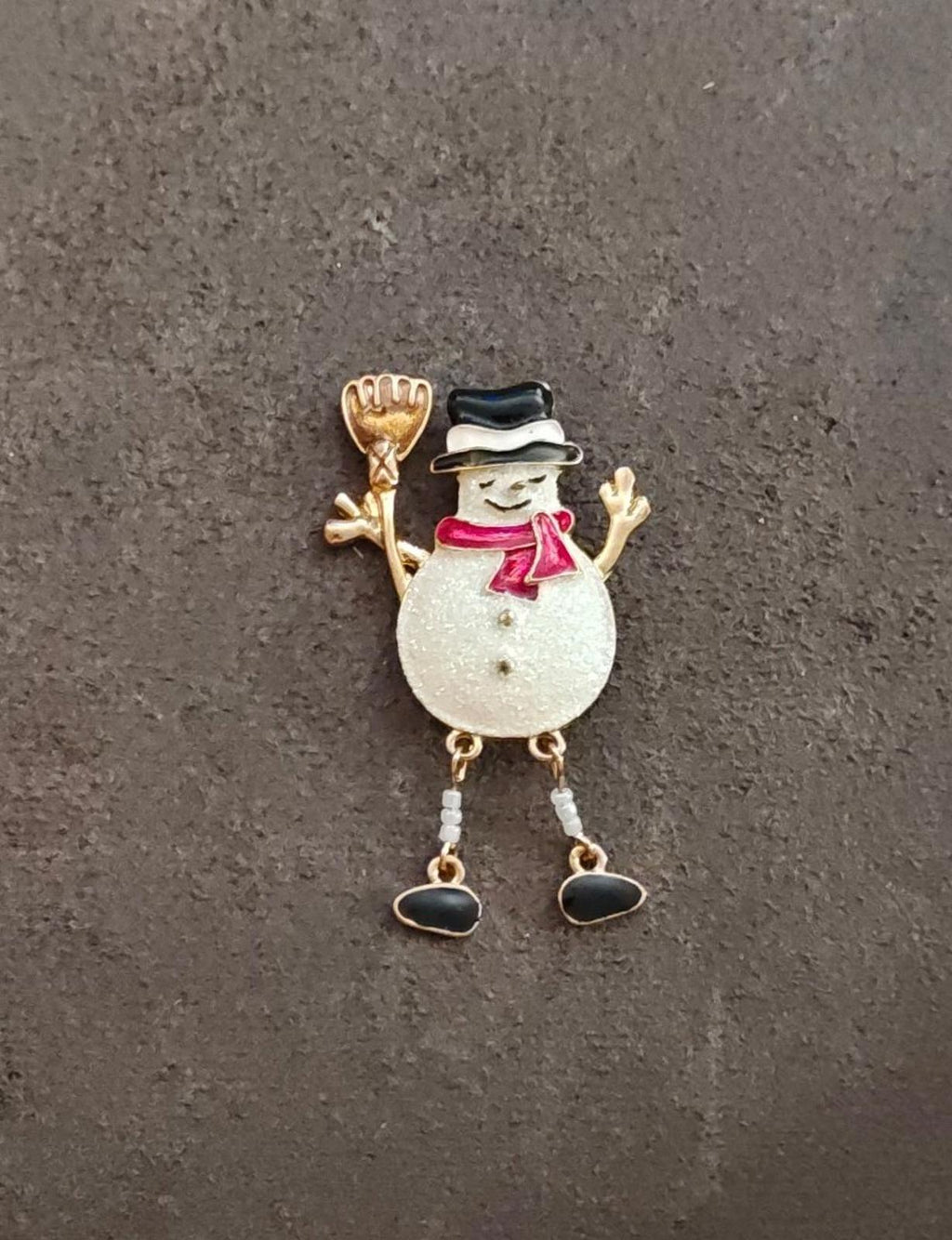 Gold tone snowman enamel brooch on dark background, red scarf and dangling bead legs.