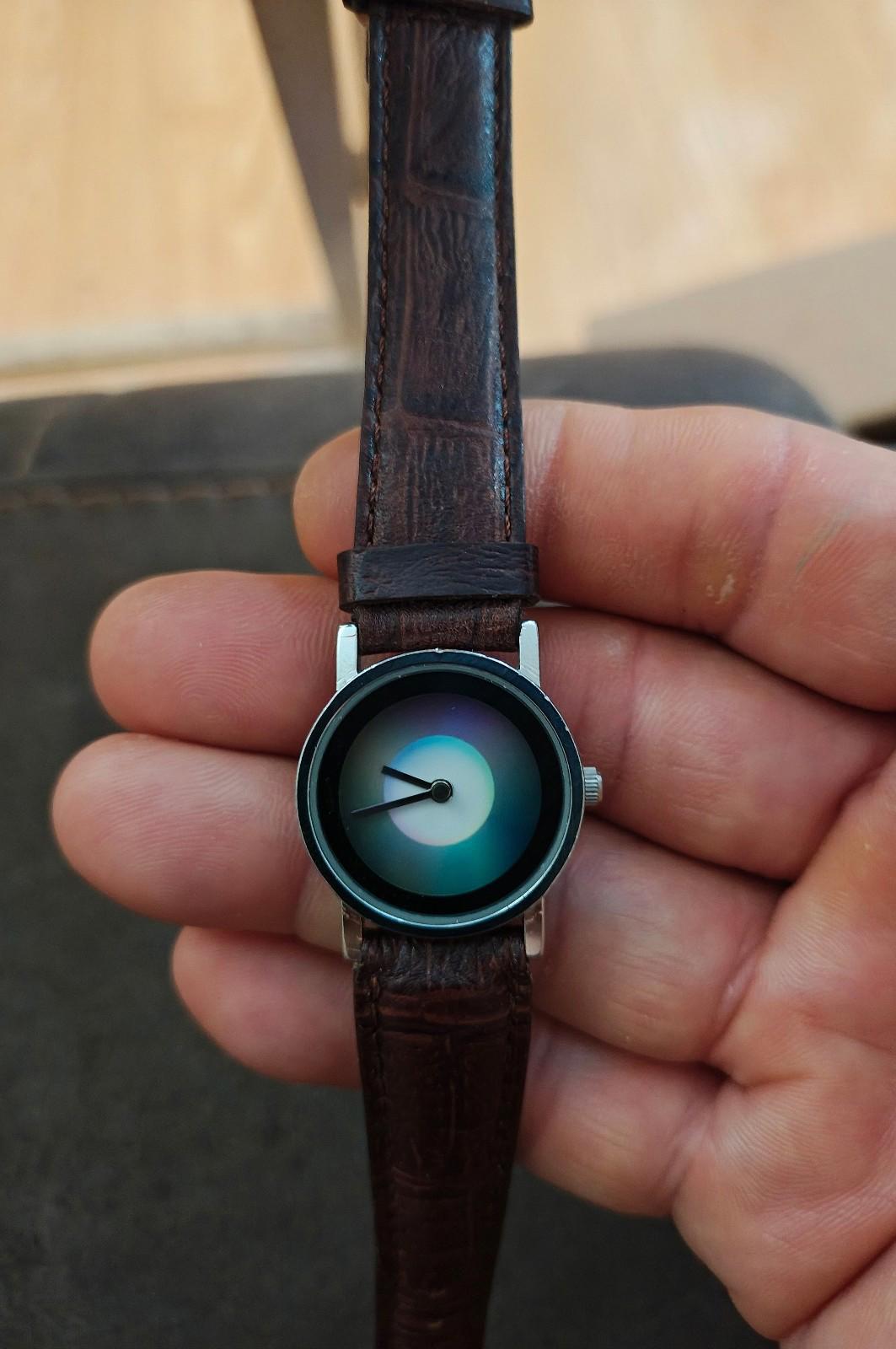 Round dial wristwatch with iridescent blue-green face, black bezel, brown leather strap