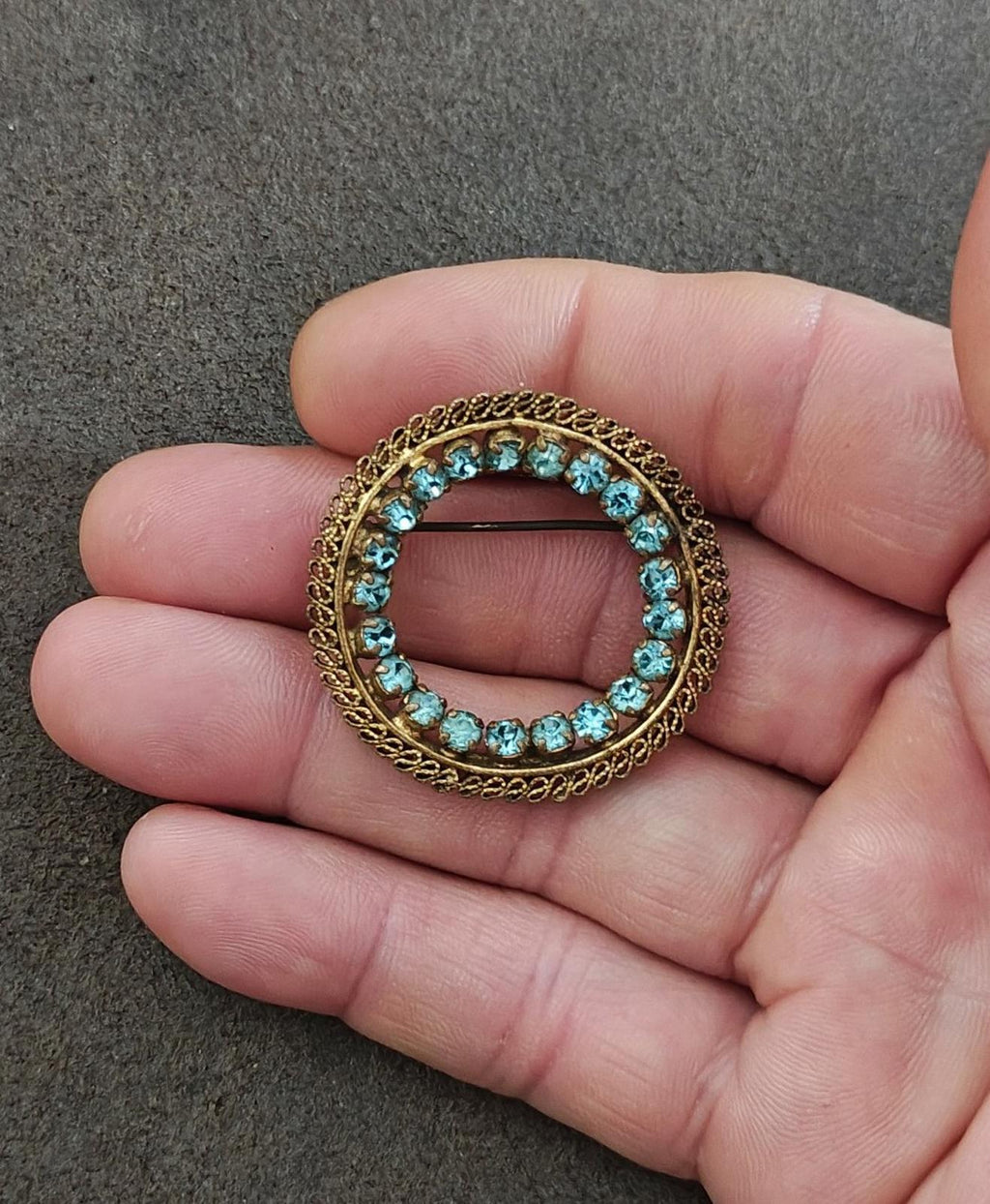 Round gold-tone brooch featuring blue stones around a center opening