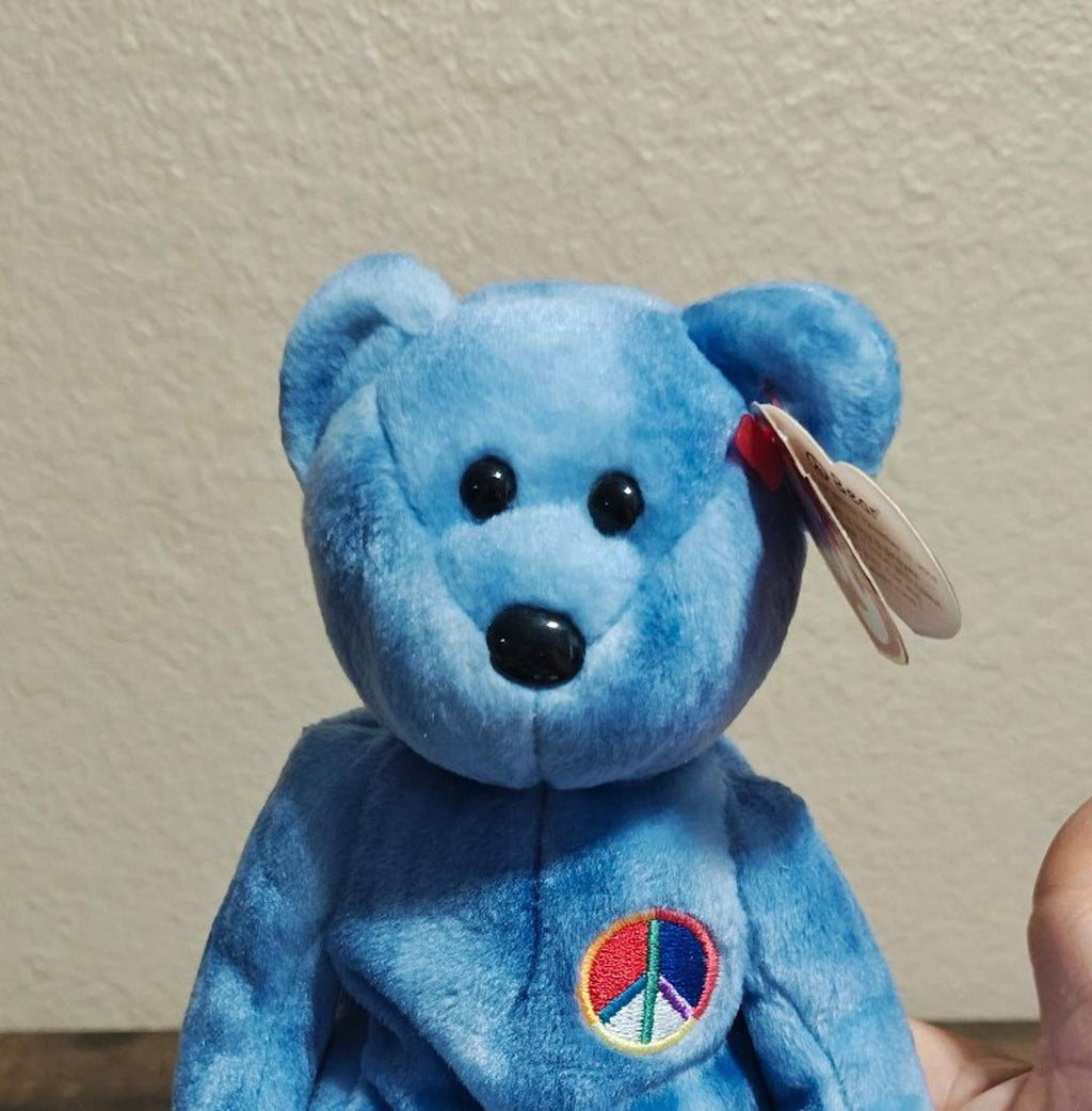 Blue bear plush face close-up with peace symbol patch on the chest and hanging tag