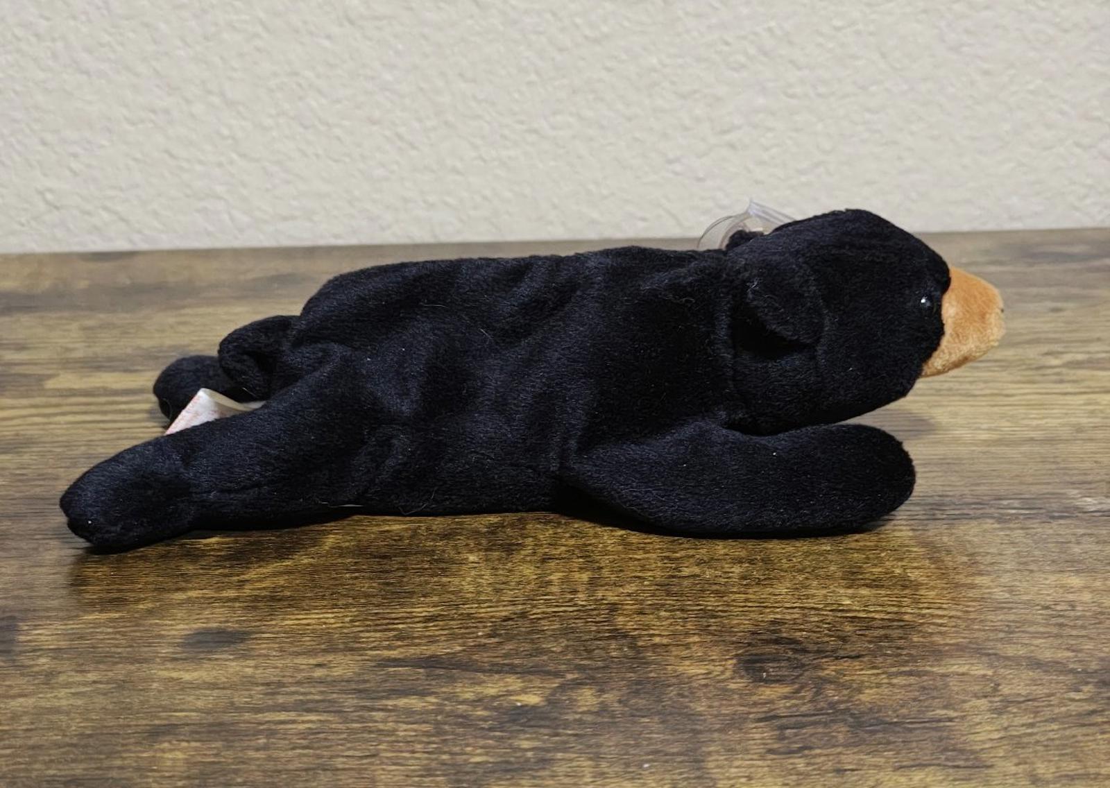 Black plush bear beanbag lying on its side, tan ear and muzzle peeking out