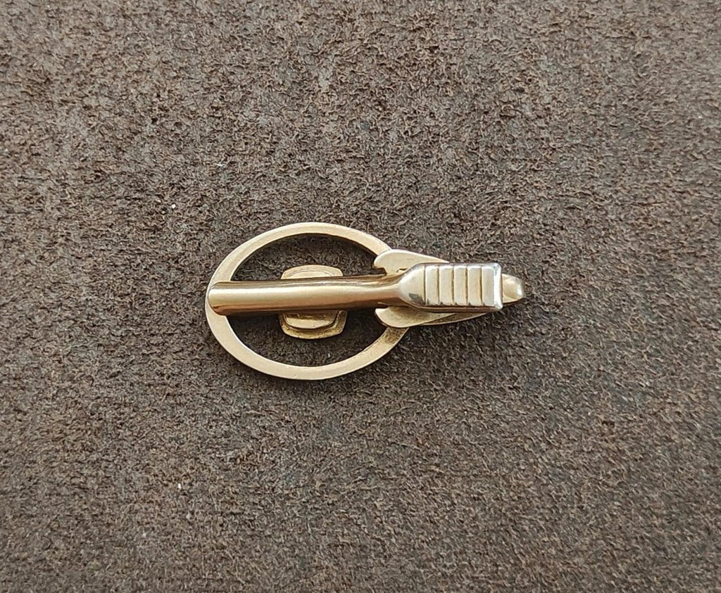 Gold-tone tie clip side view with circular frame and ribbed bar detail