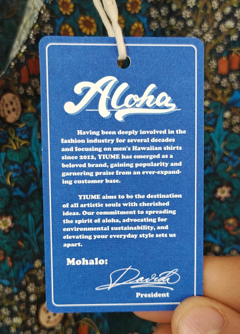 Blue floral Hawaiian shirt with blue hang tag text reading “Aloha” and “Mahalo”
