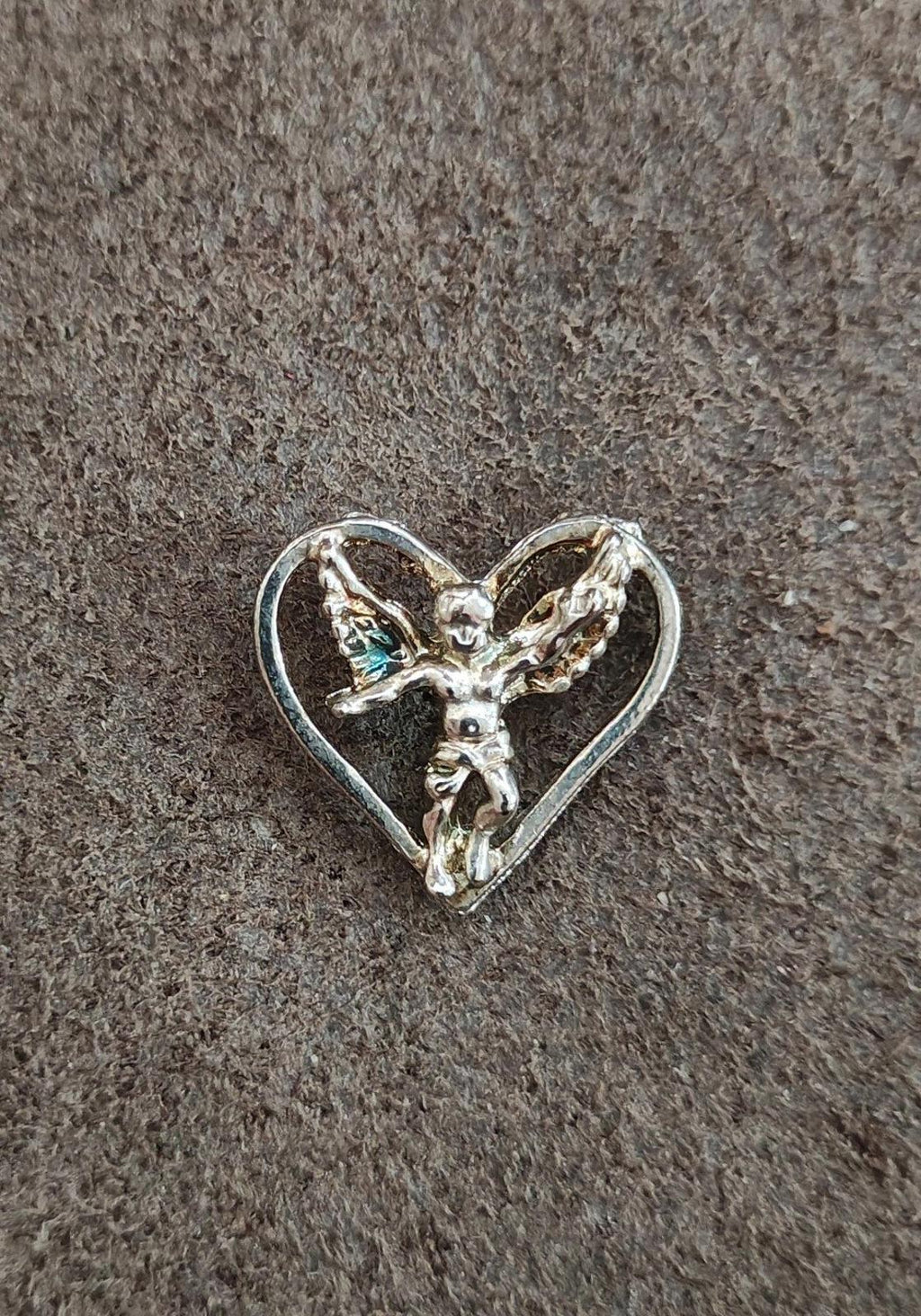 Silver-tone heart pin featuring a winged angel figurine, viewed on dark fabric