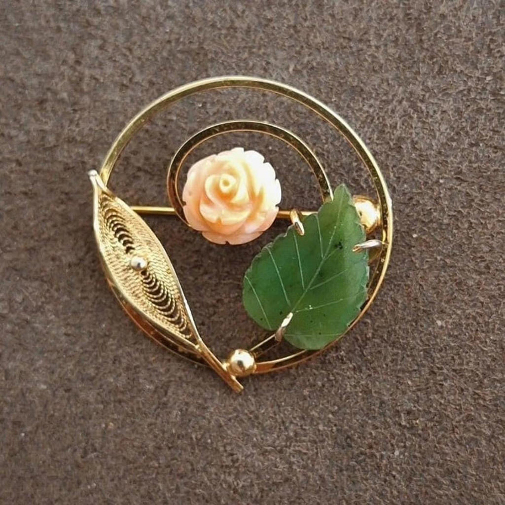 Gold-tone filigree brooch with pale rose center and green leaves on a round frame.