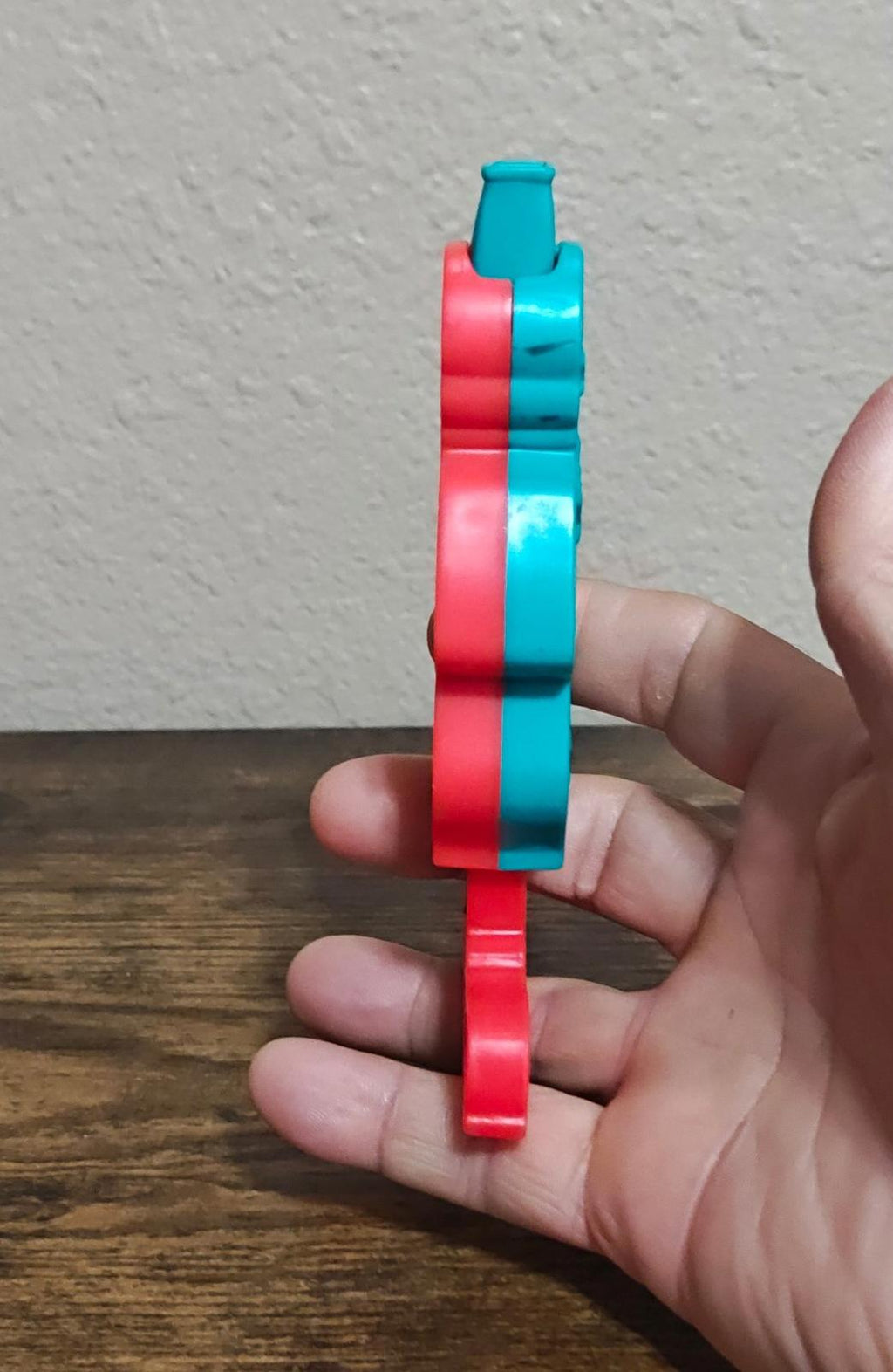 Side view of slide whistle bands: teal and red plastic pieces stacked on a handle.