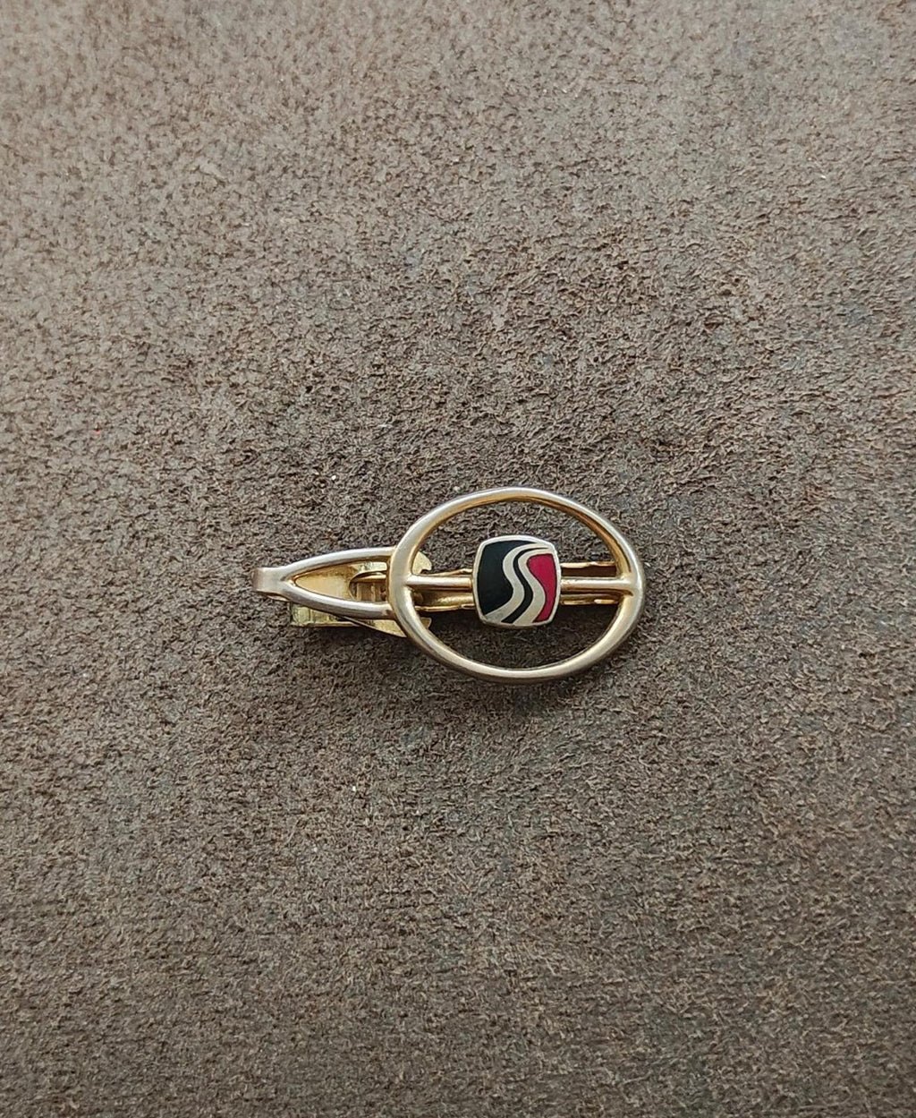 Gold-tone highway tie clip on gray surface with circular ring and black enamel wavy center
