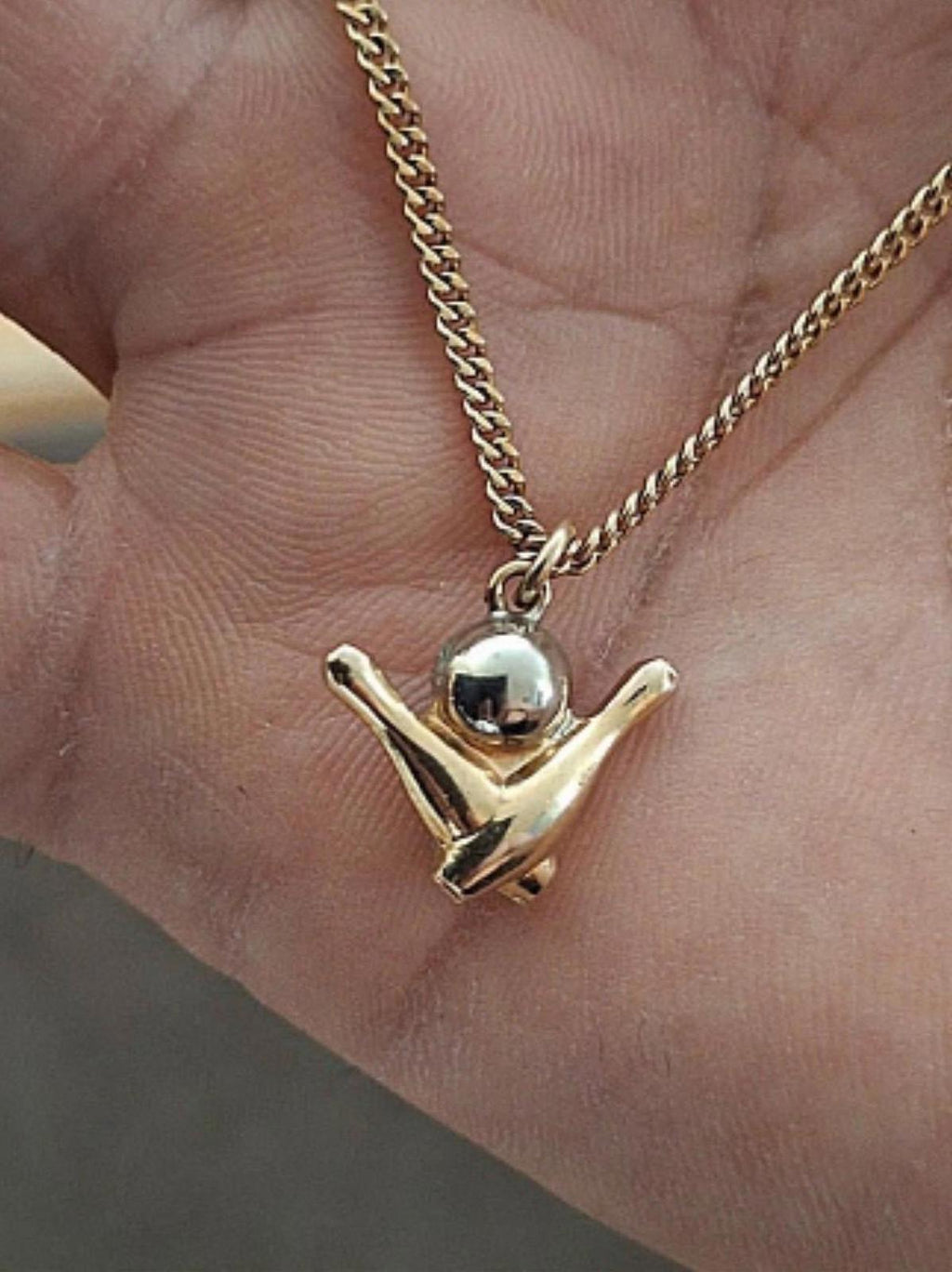 Gold-tone bowling pin charm pendant and chain over open palm.