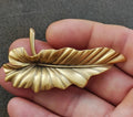 Gold-tone leaf brooch pin with textured veins and raised center, pointed clasp.