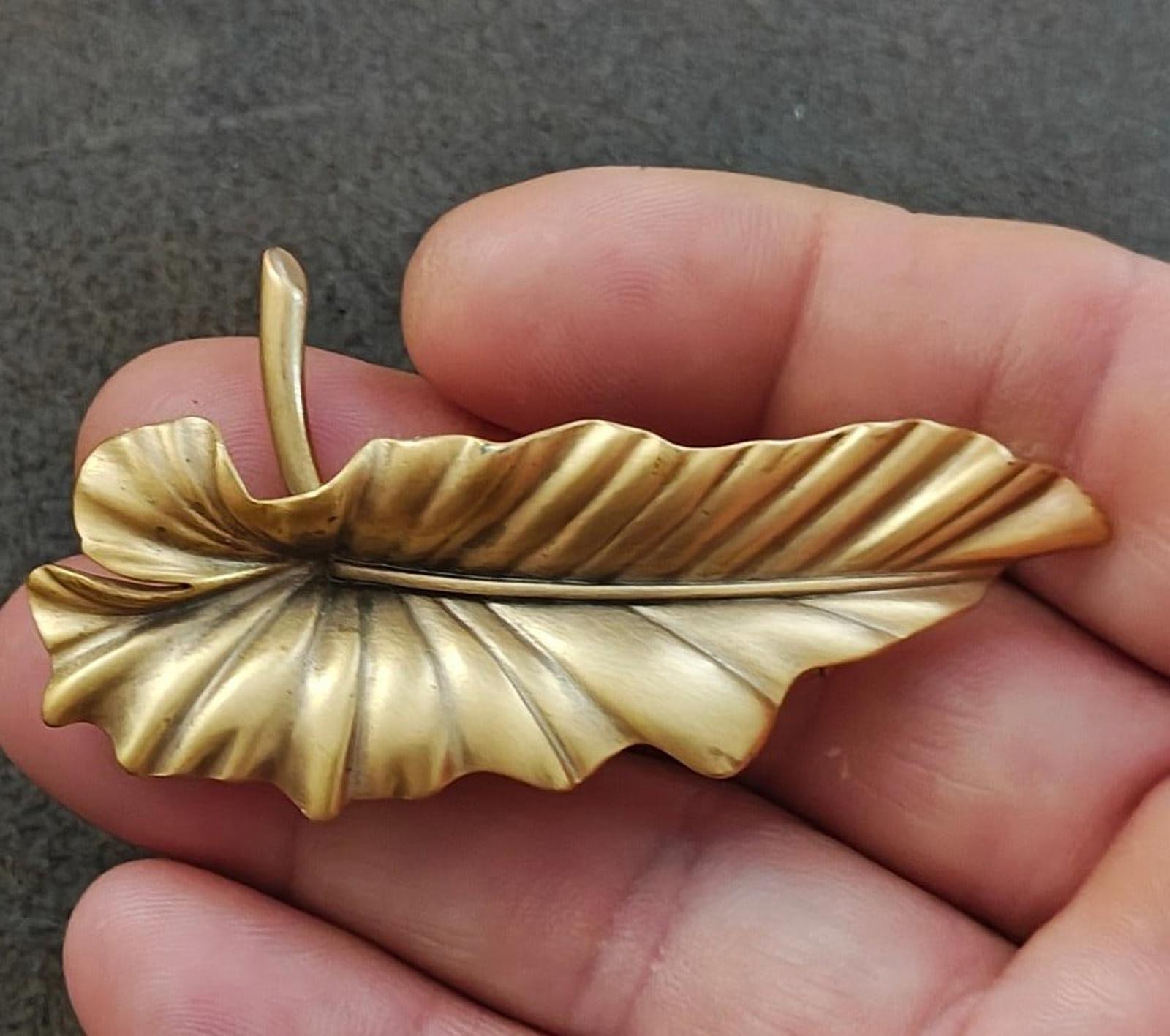 Gold-tone leaf brooch pin with textured veins and raised center, pointed clasp.