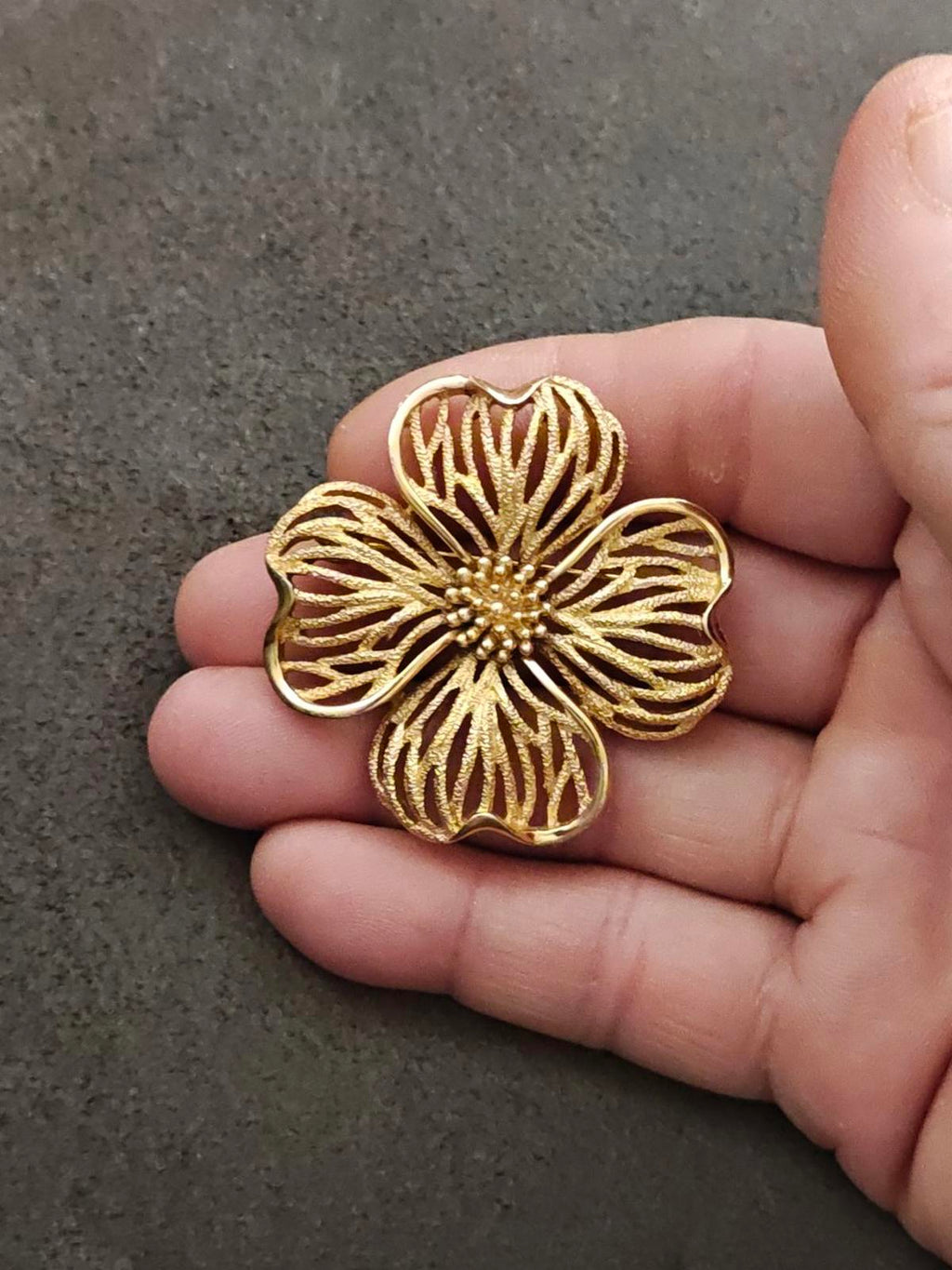 Gold-tone dogwood flower brooch with ridged petals and beaded center, held up