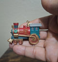 Blue and red train locomotive ornament with gold trim, spinning wheel detail, hanging loop