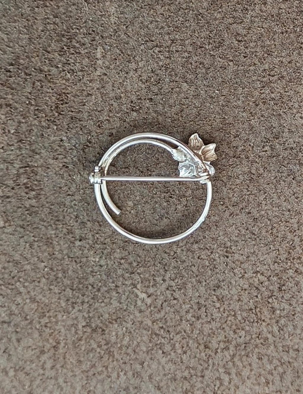 Silver round brooch with floral accent and bar pin across the front