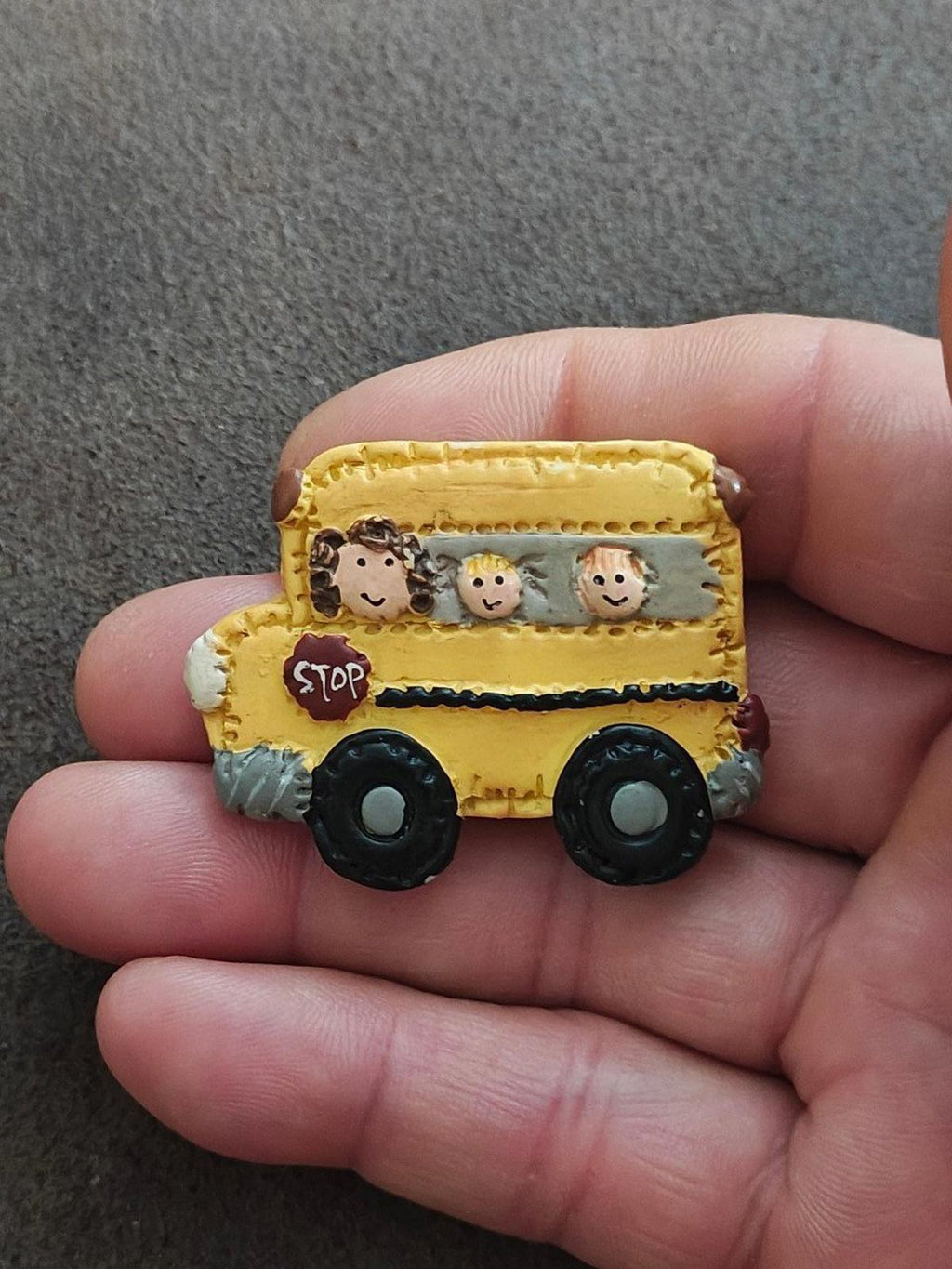 Yellow school bus resin pin held in hand, cartoon kids in window and red STOP sign